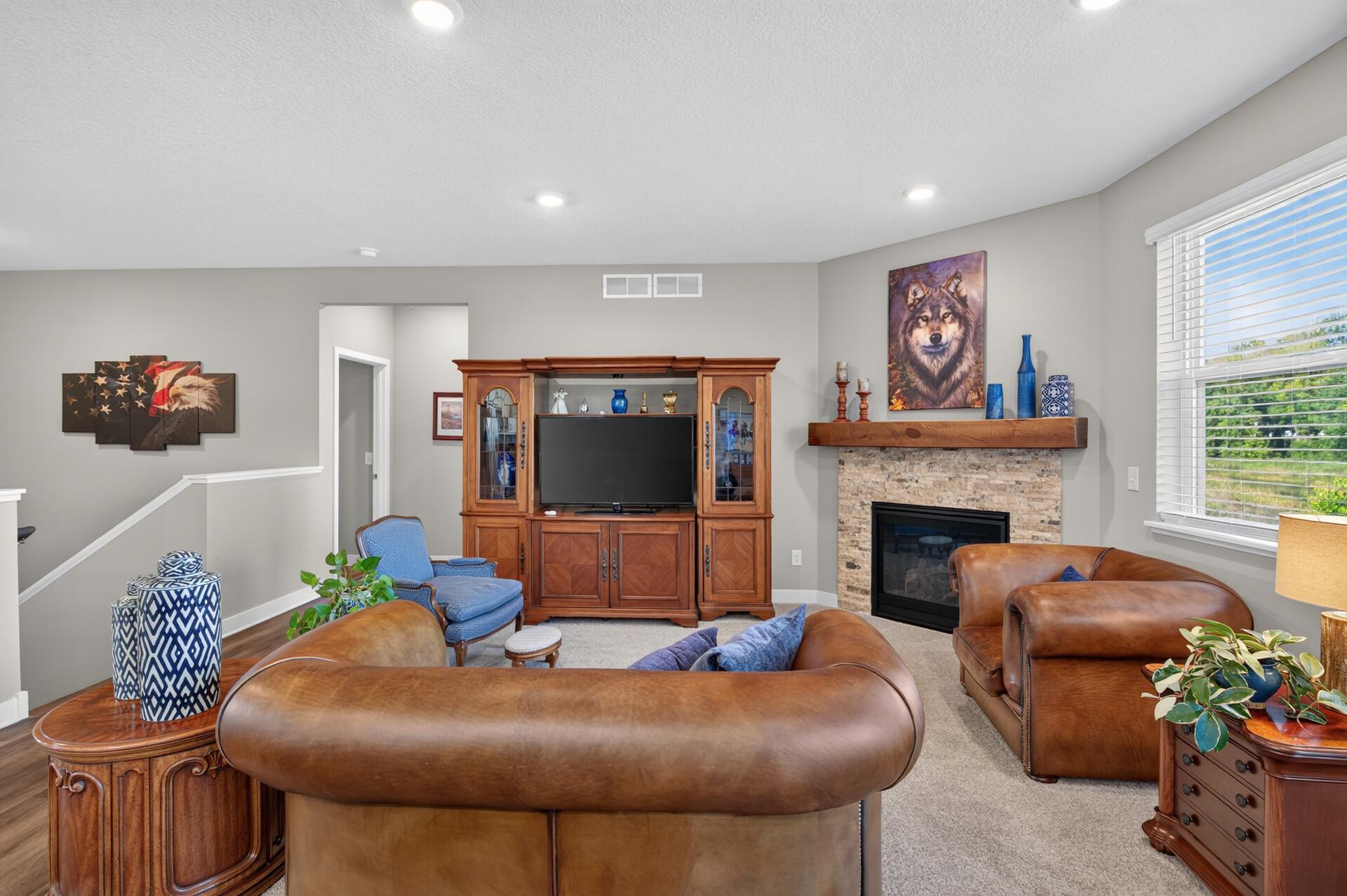 Living room with brown leather seating, stone fireplace, and wooden entertainment cabinet.