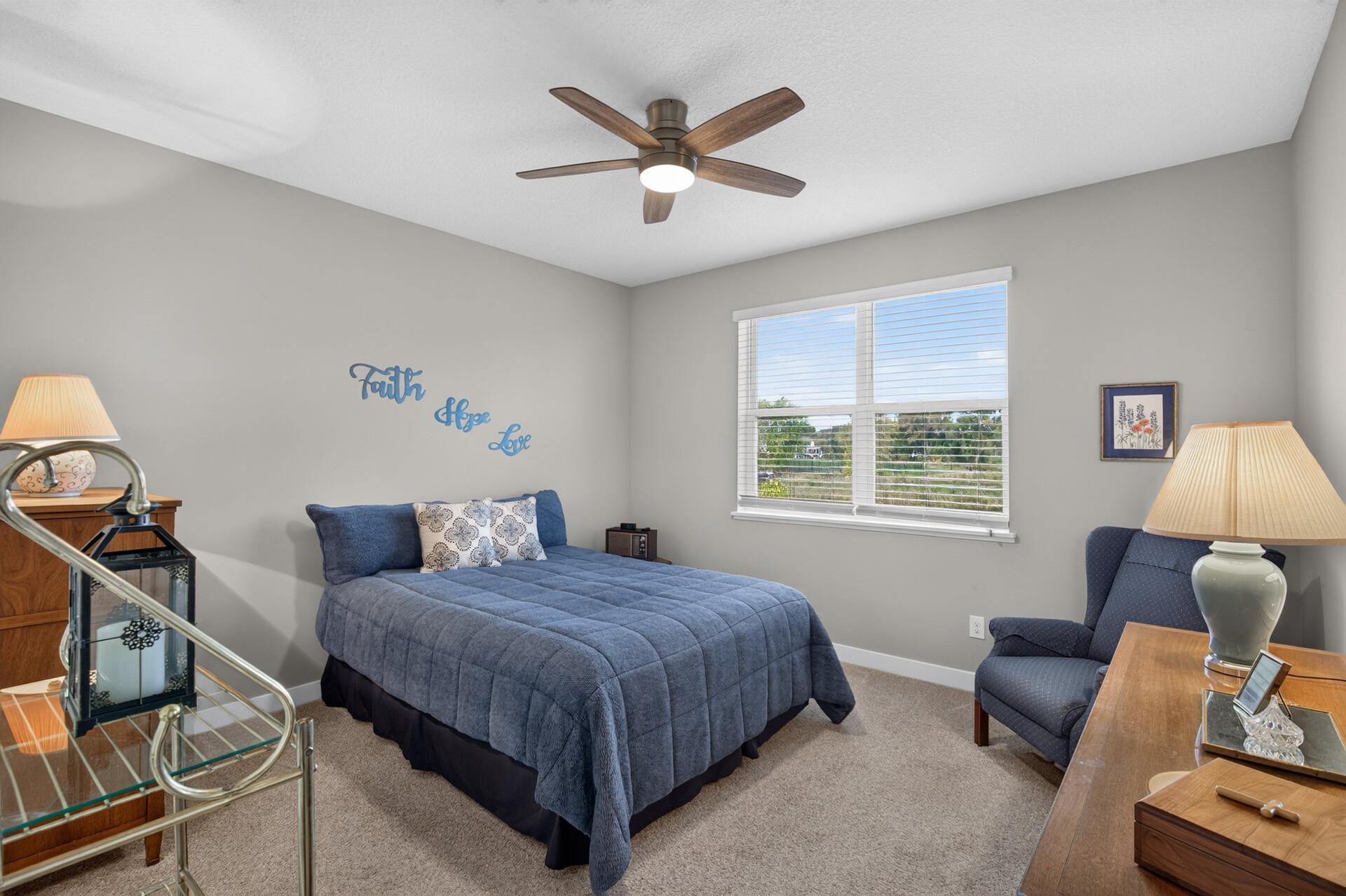 Bedroom with a blue quilted bed, blue armchair, and window with white blinds.