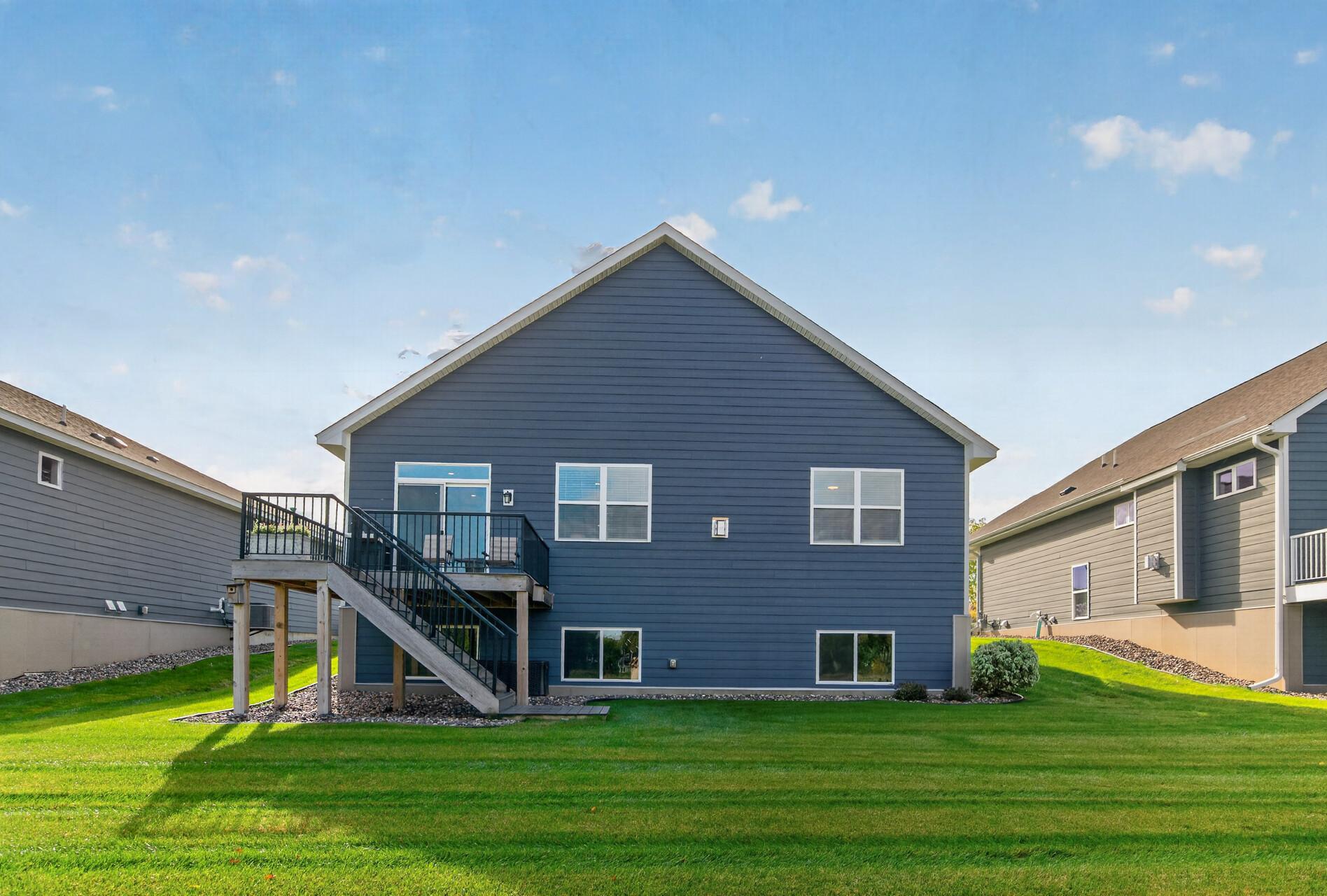 Blue-sided home's rear exterior with a raised deck and stairs overlooking a broad green lawn.