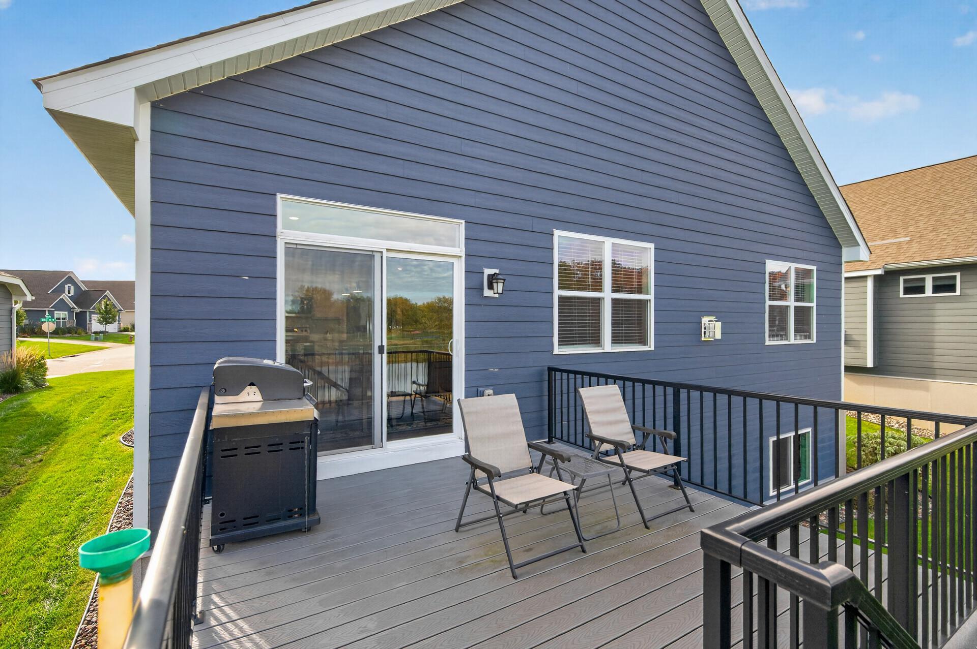 Elevated deck with patio chairs and grill beside a blue-sided home