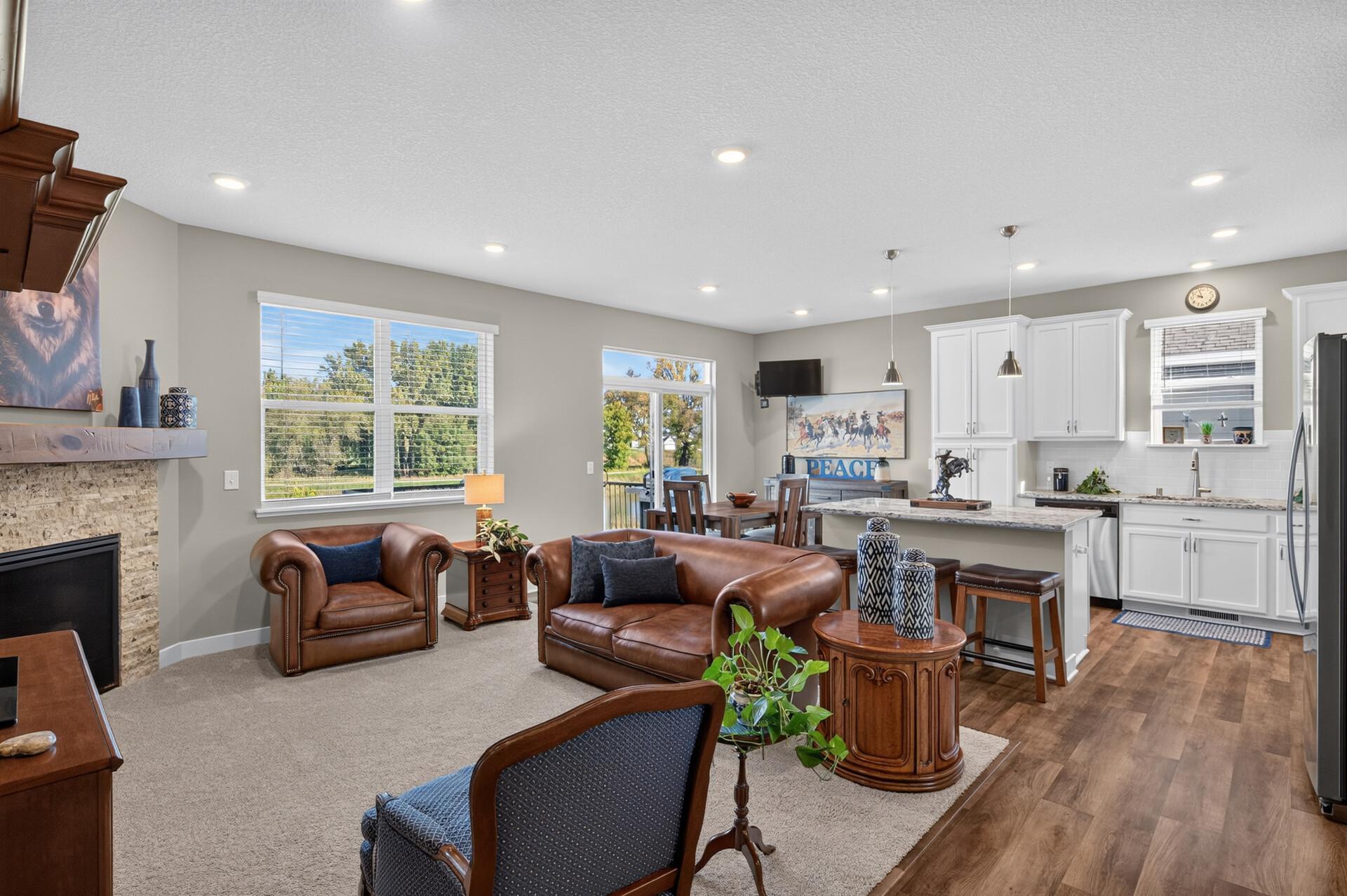Open-plan living room and kitchen with brown leather seating, a stone fireplace, and white cabinets.