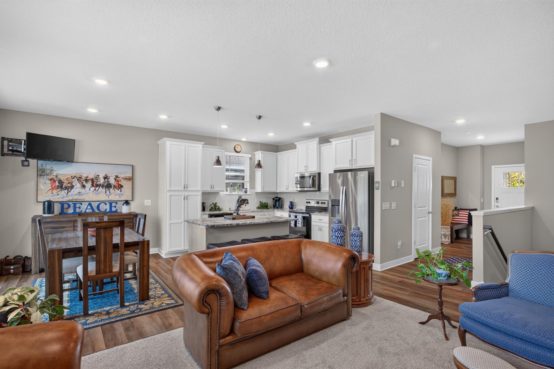 Open-plan living room and kitchen with white cabinets, granite island, and brown leather sofas.