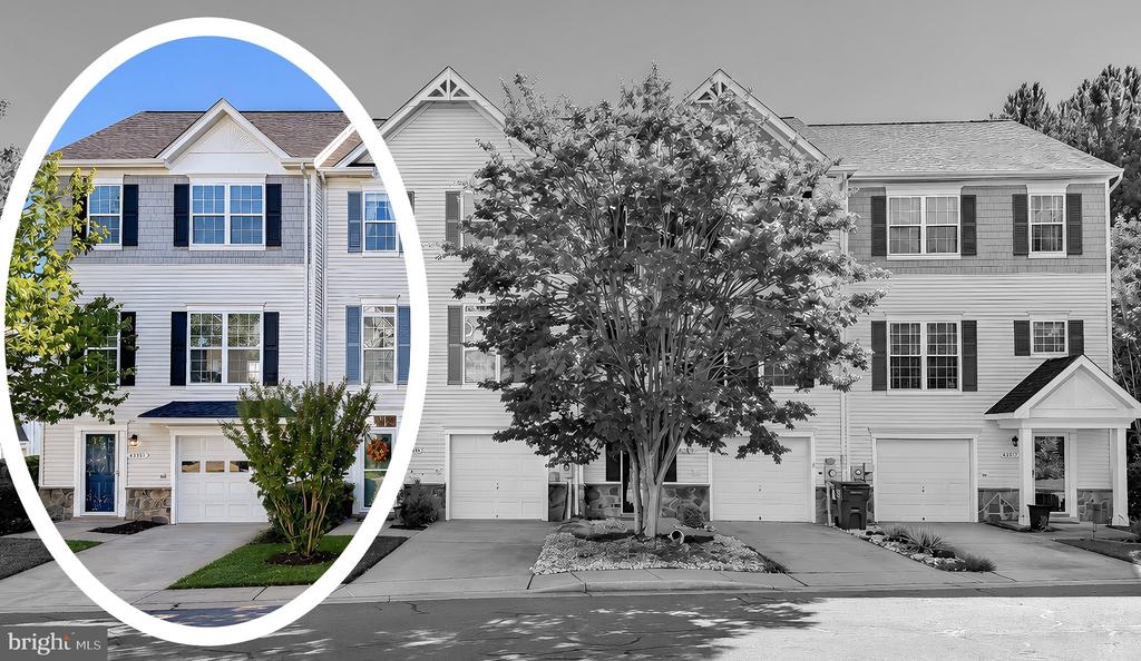 White-sided townhouse with black shutters and an attached garage, highlighted in color among neighboring homes.
