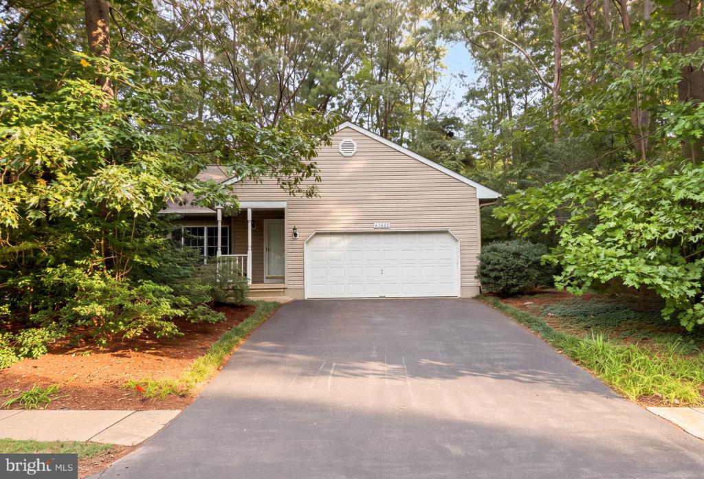 Beige-sided home with a white double garage, wide driveway, and mature trees surrounding the front yard.