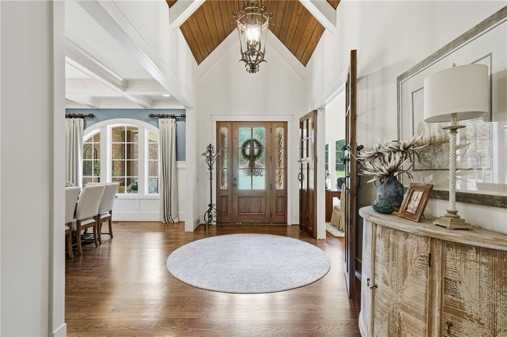 Entry foyer with vaulted ceilings, wood-paneled accents, a glass-front wooden door, and round rug.