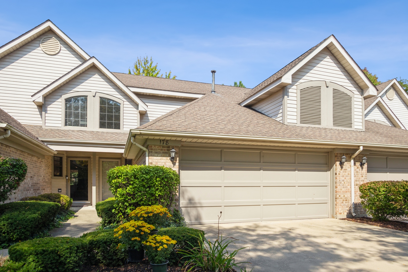 Two-story home with a large attached garage, peaked dormers, and landscaped front garden.