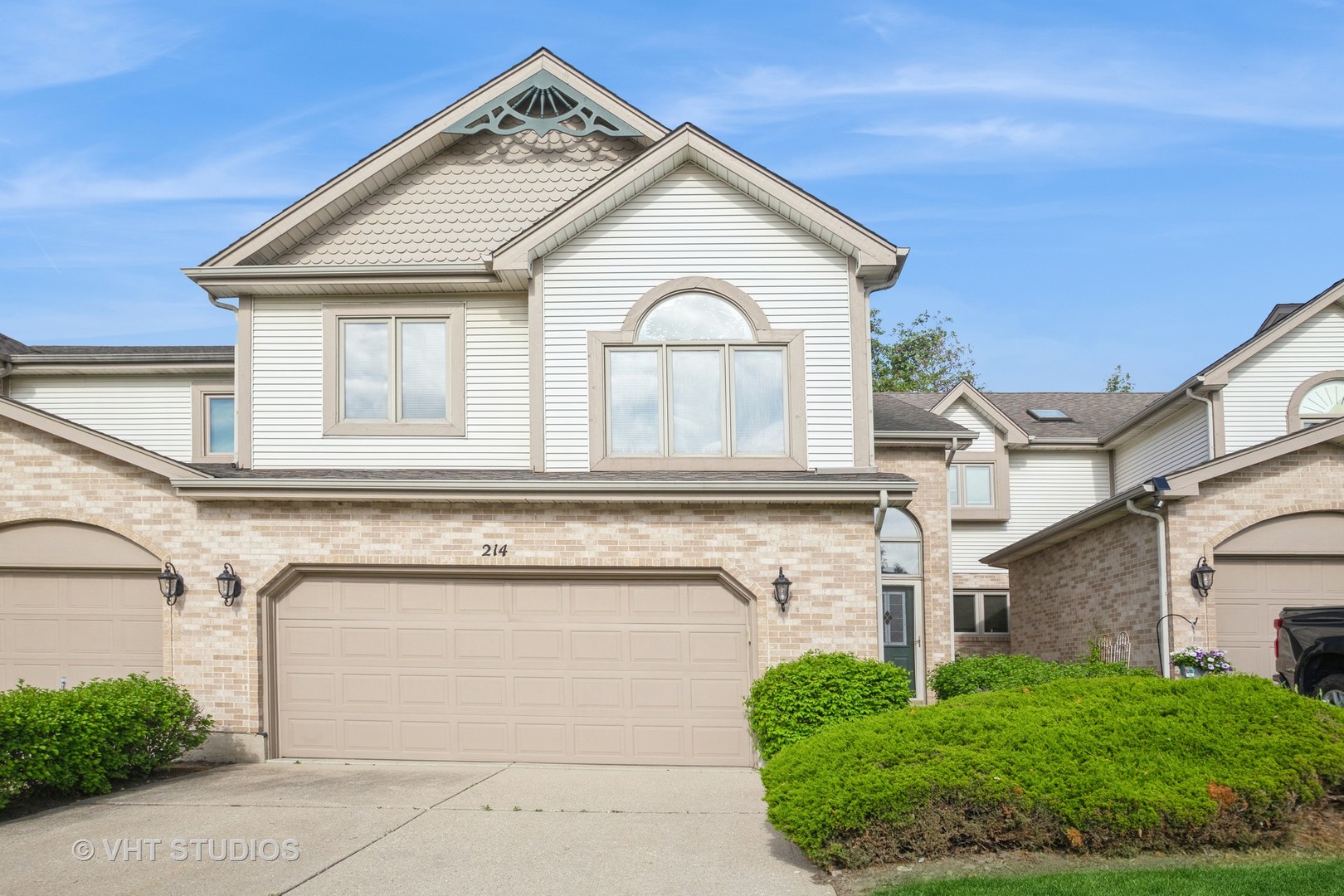 Two-story attached home with decorative gables, a wide garage, and landscaped shrubs.