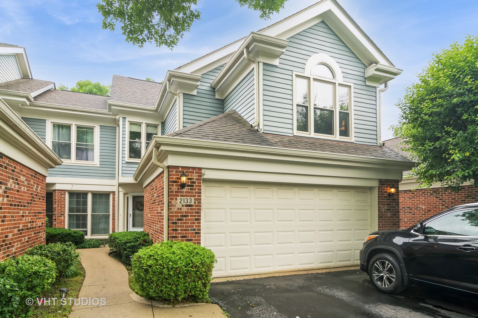 Two-story blue-gray house with brick accents, a double garage, and landscaped front walkway.