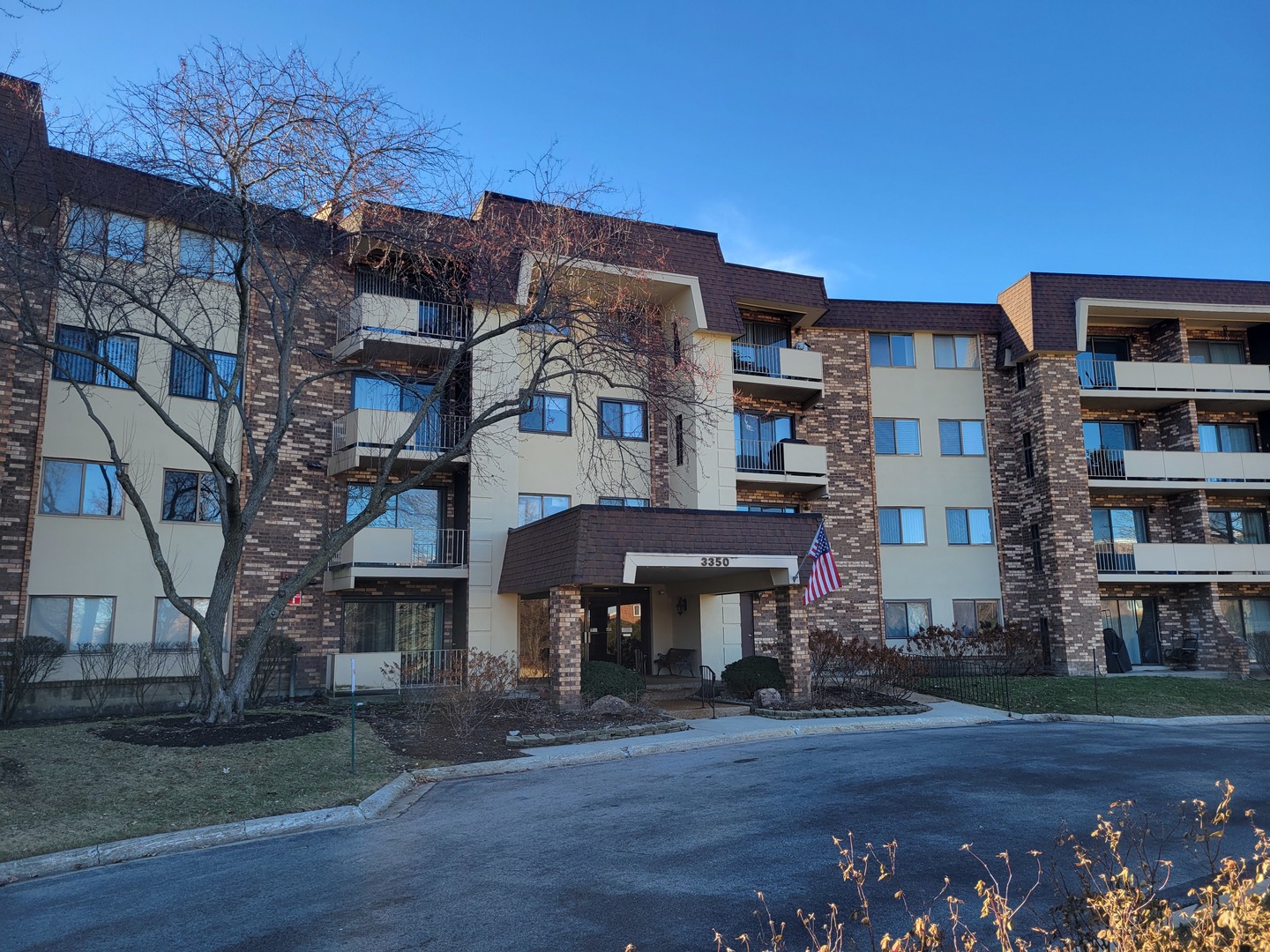Multi-story apartment building with balconies, a covered entrance, and an American flag.