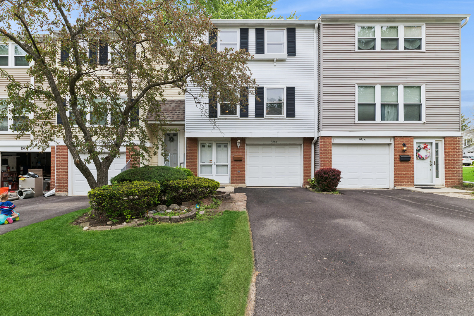 Townhouse at 1813 with an attached garage, brick façade, front lawn, and mature shade tree.