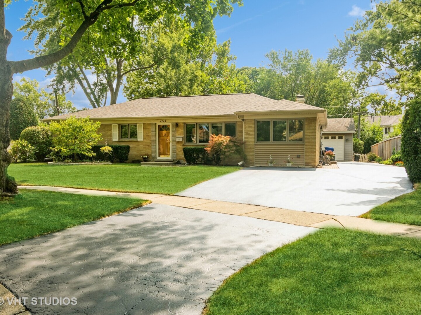 Single-story brick ranch with an attached garage, broad driveway, and mature trees.