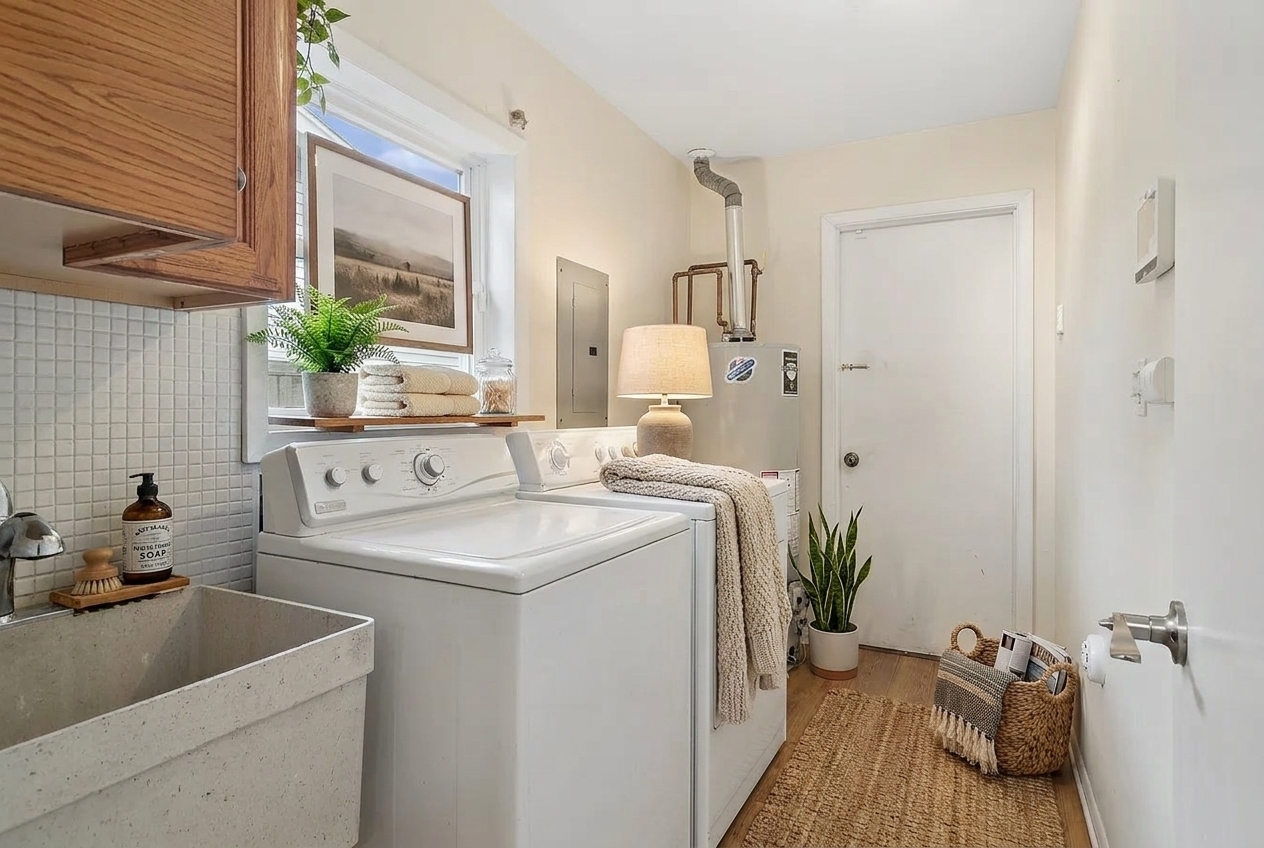 Laundry room with white washer and dryer, deep sink, wood cabinets, and woven runner.