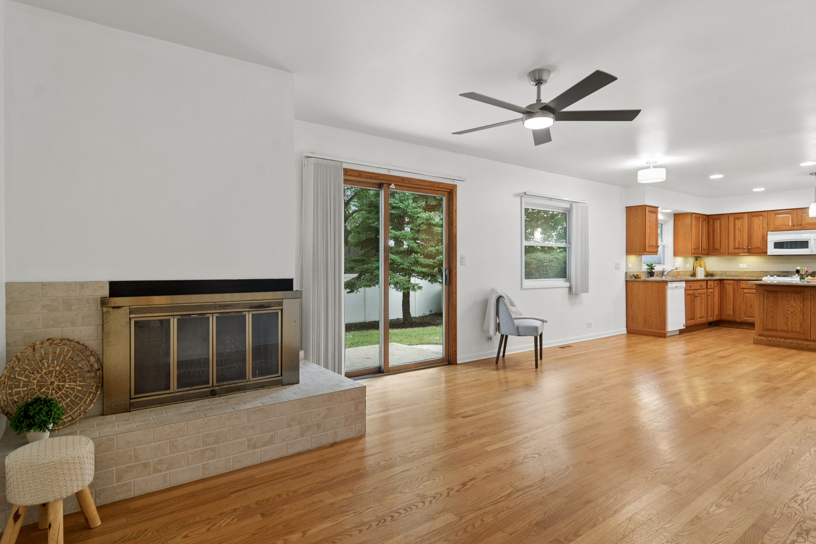 Living room with tiled fireplace, hardwood floors, sliding glass doors, and an adjoining wood-cabinet kitchen.