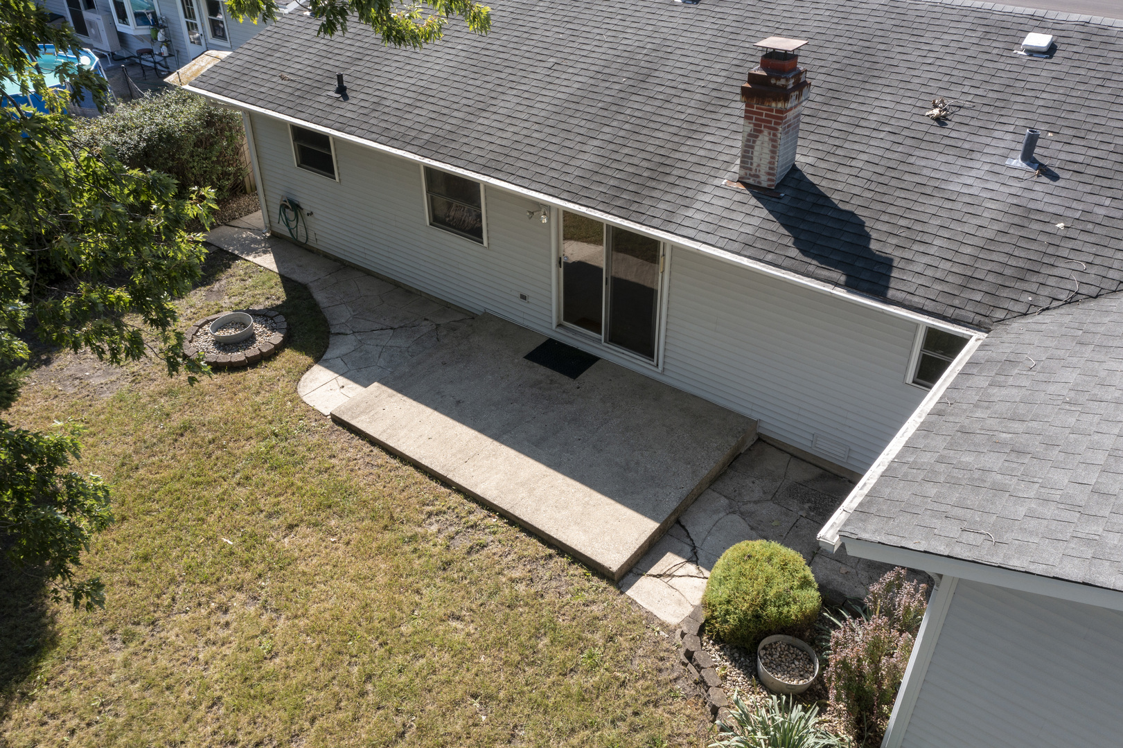 Rear of a light-sided house with a concrete patio, sliding doors, and a broad shingled roof.