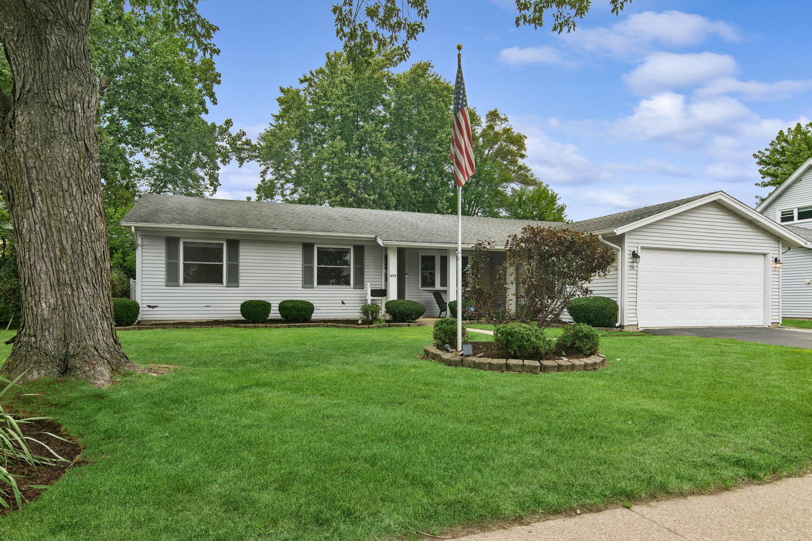 Single-story white house with an attached garage, broad lawn, and American flag.