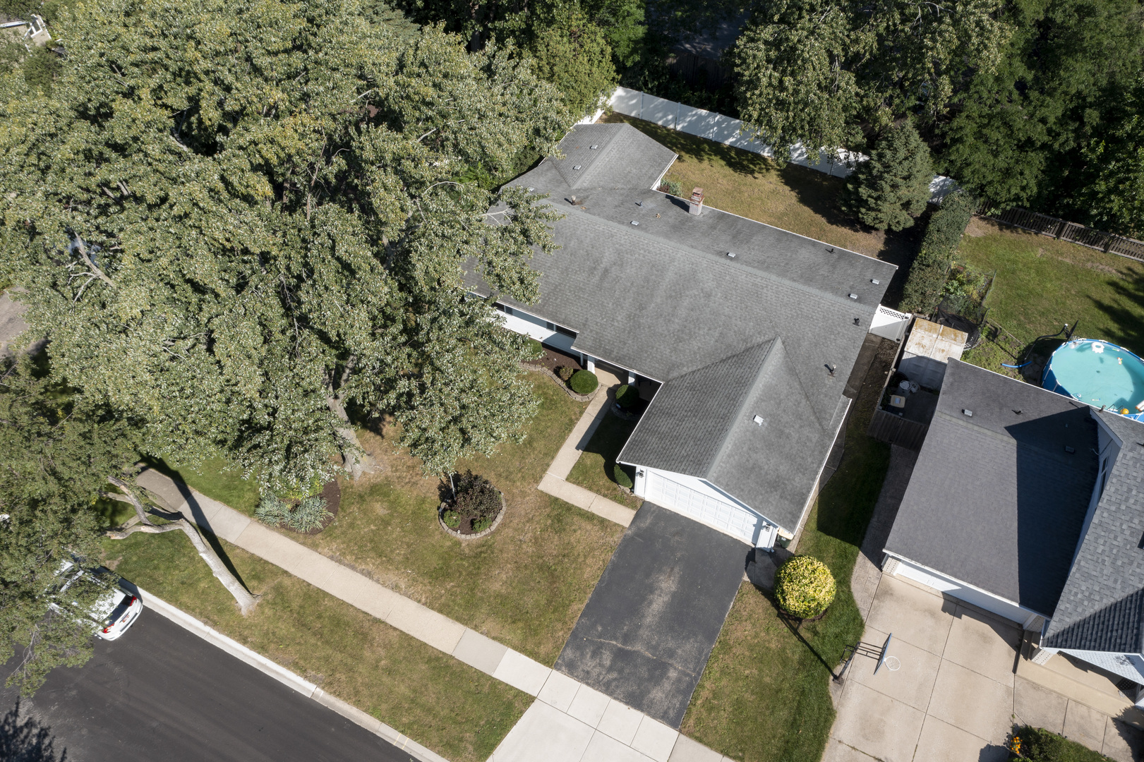 Aerial view of a single-story home with an attached garage, mature trees, and a long driveway.