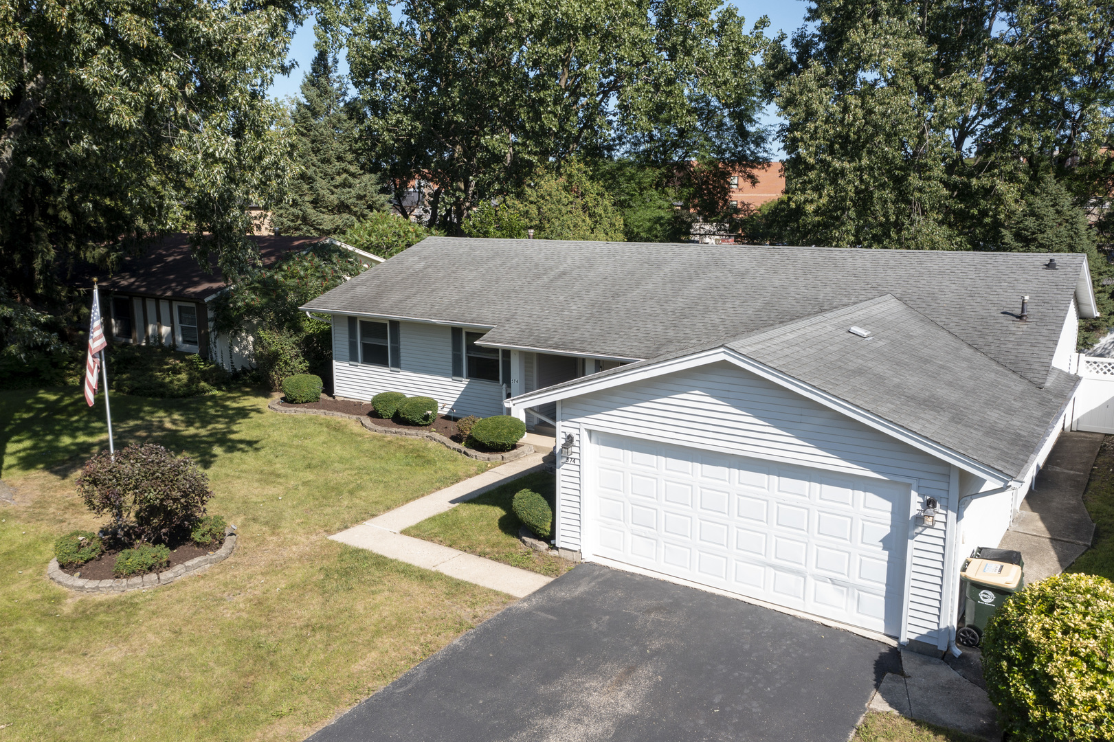 Single-story light-blue home with an attached two-car garage, front lawn, and American flag.