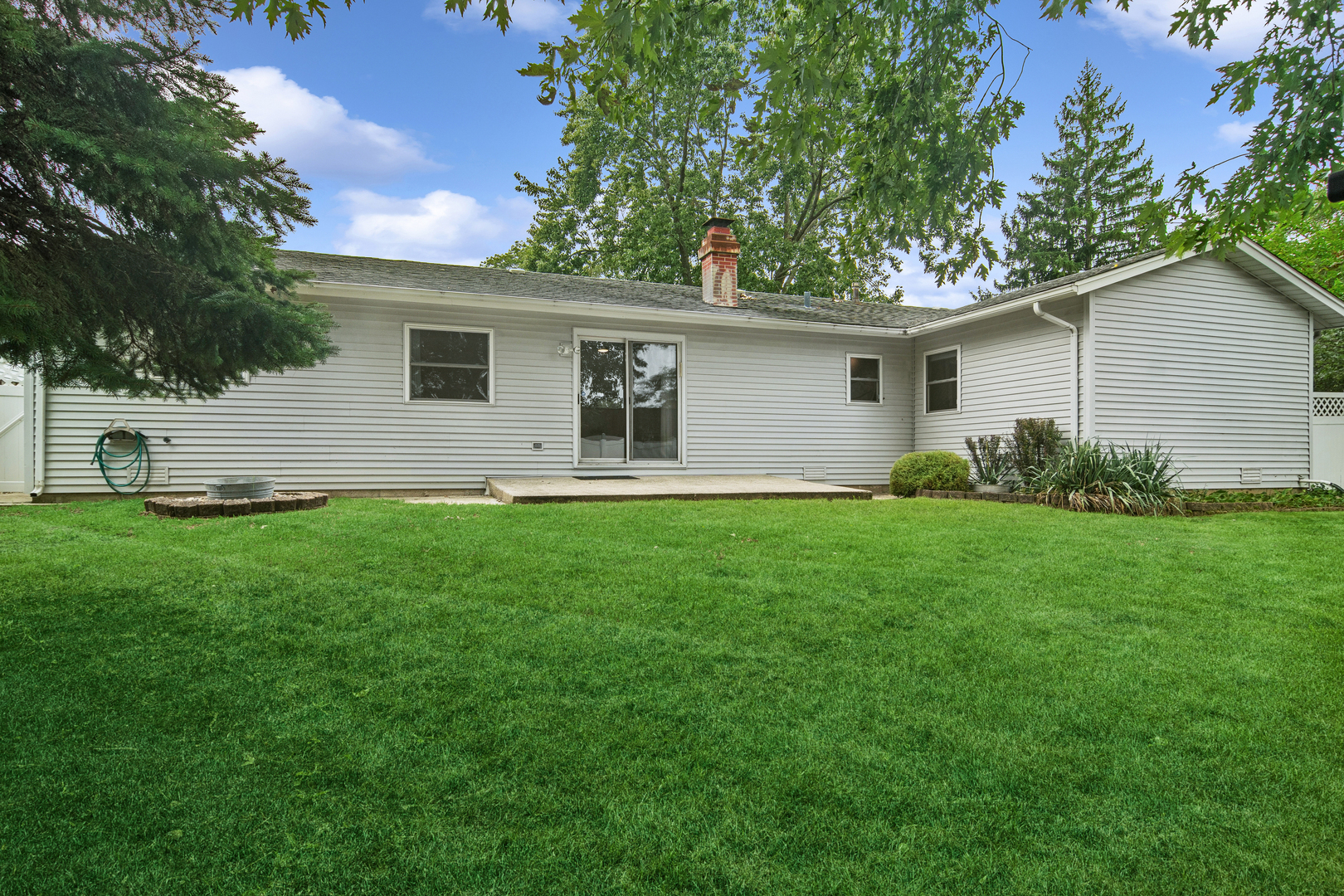 Rear of a single-story house with a brick chimney, sliding doors, and a broad green lawn.