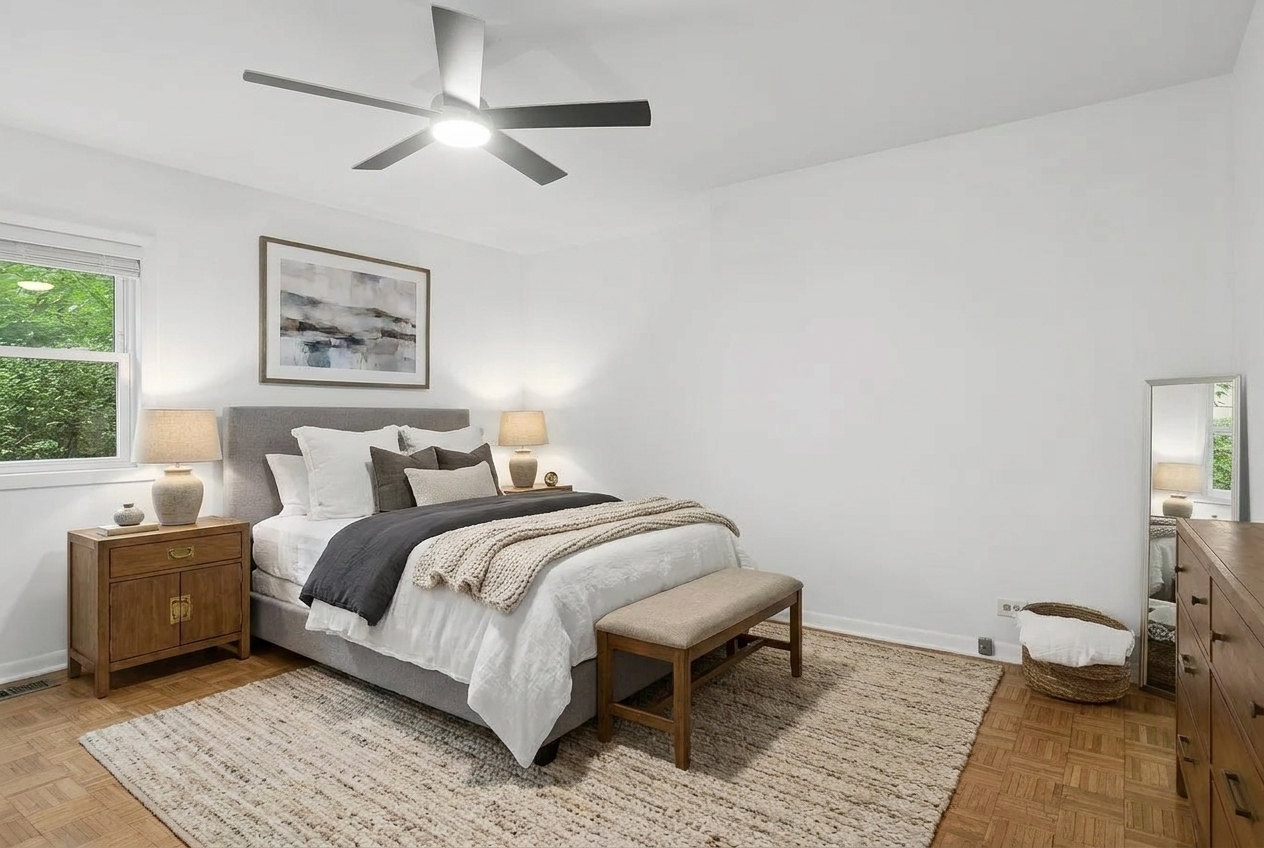Staged bedroom with a gray upholstered bed, wood nightstands, and a cream rug over parquet flooring.