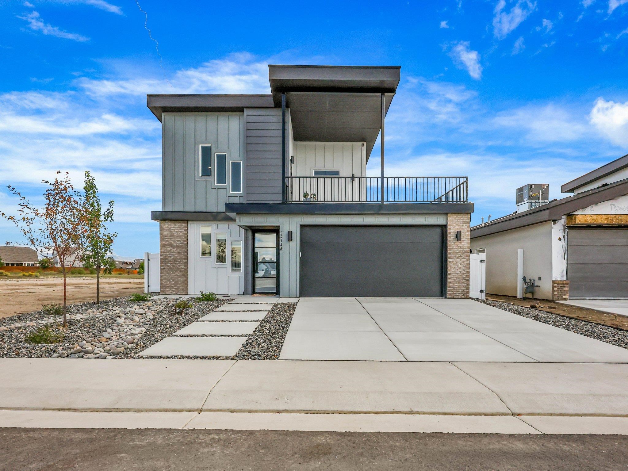 Modern gray two-story house with an upper balcony, wide garage, and landscaped driveway.