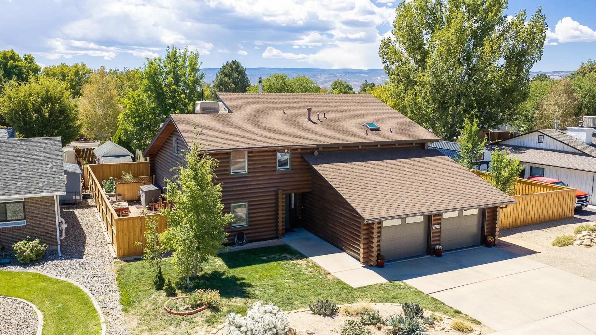 Log-style home with an attached two-car garage, fenced yard, and landscaped lawn.
