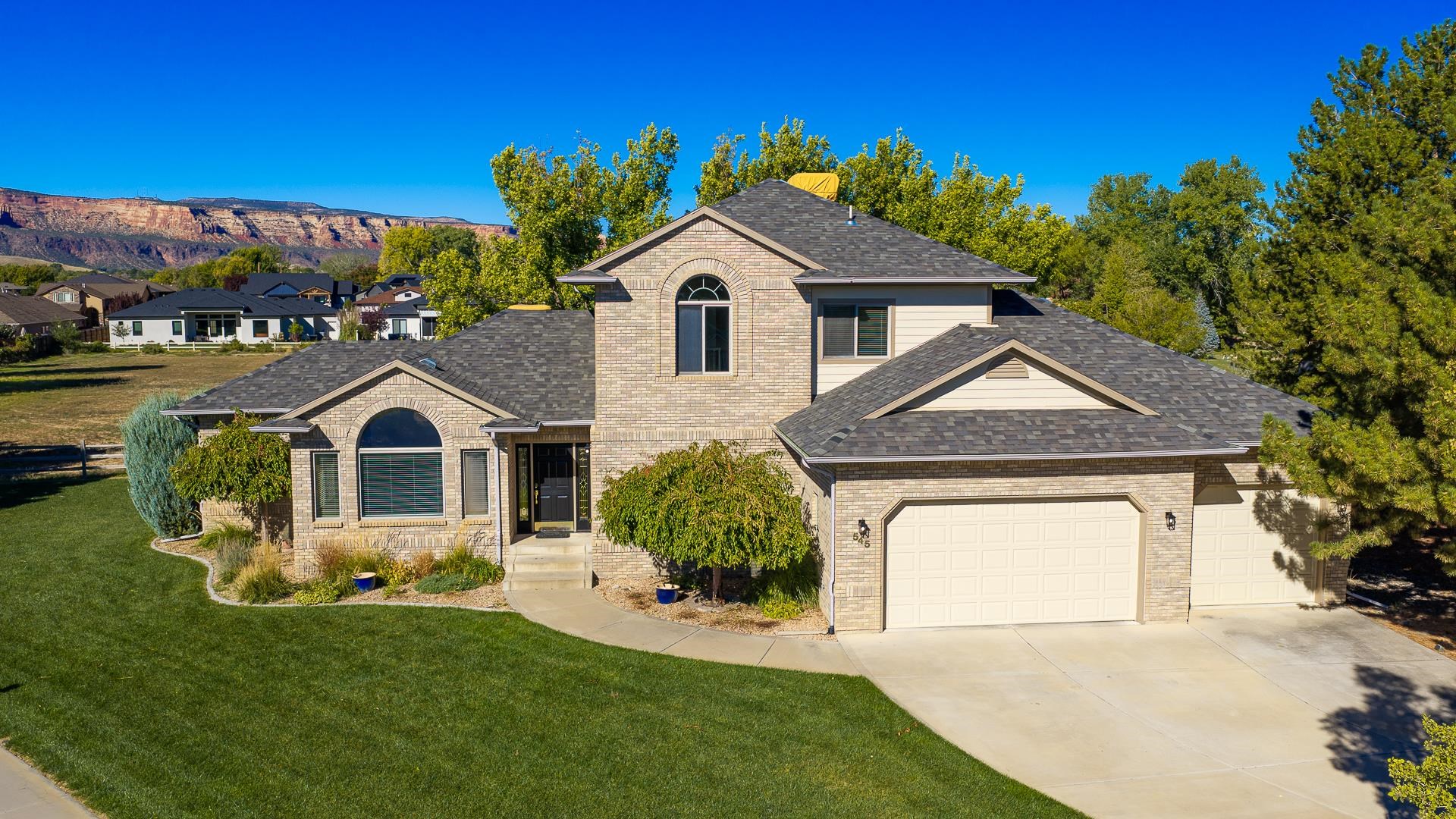 Two-story brick home with attached garages, green lawn, and red-rock mesa in the background.