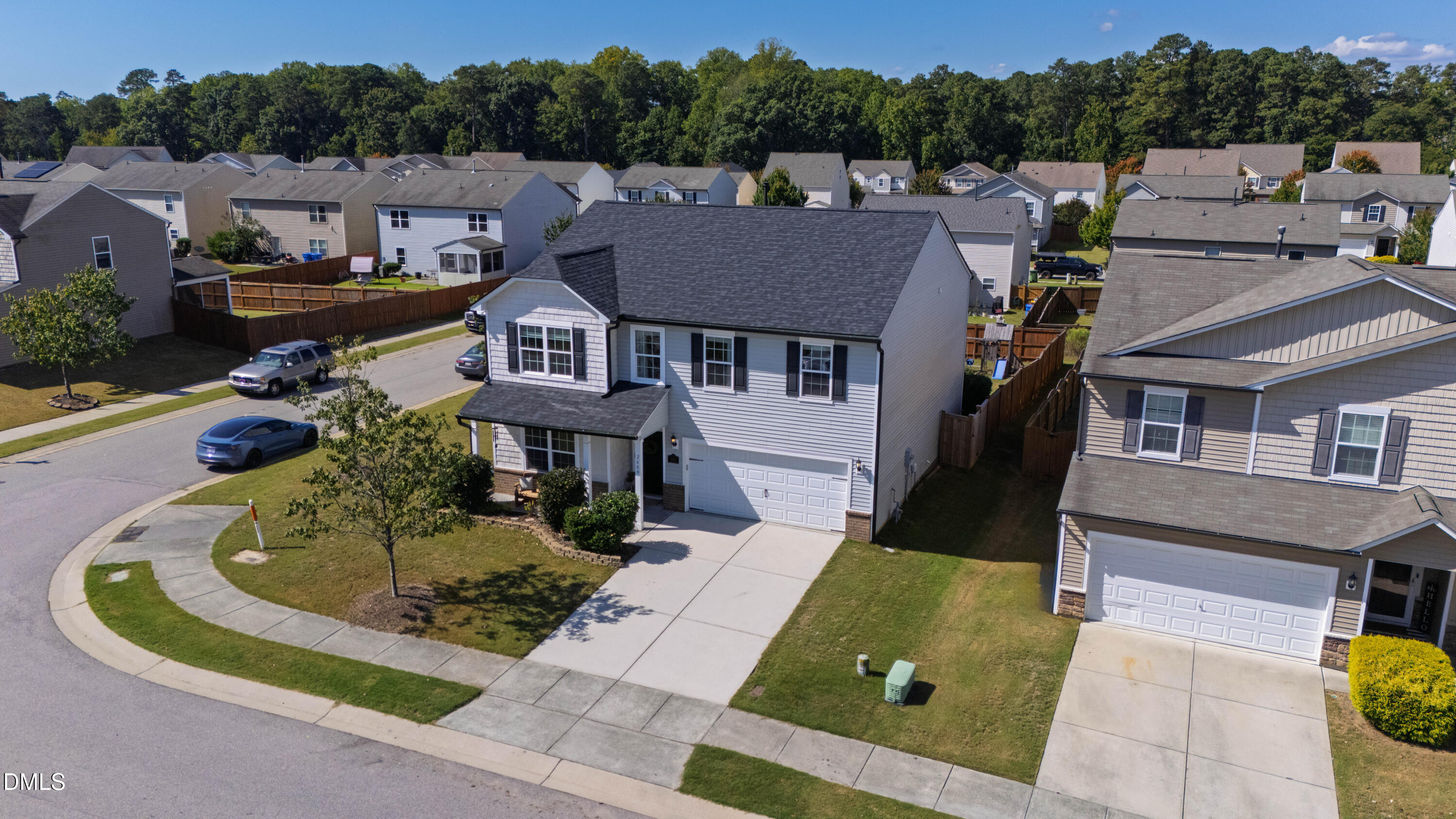 Two-story gray suburban home with a front porch and attached garage, viewed from above among neighboring houses.