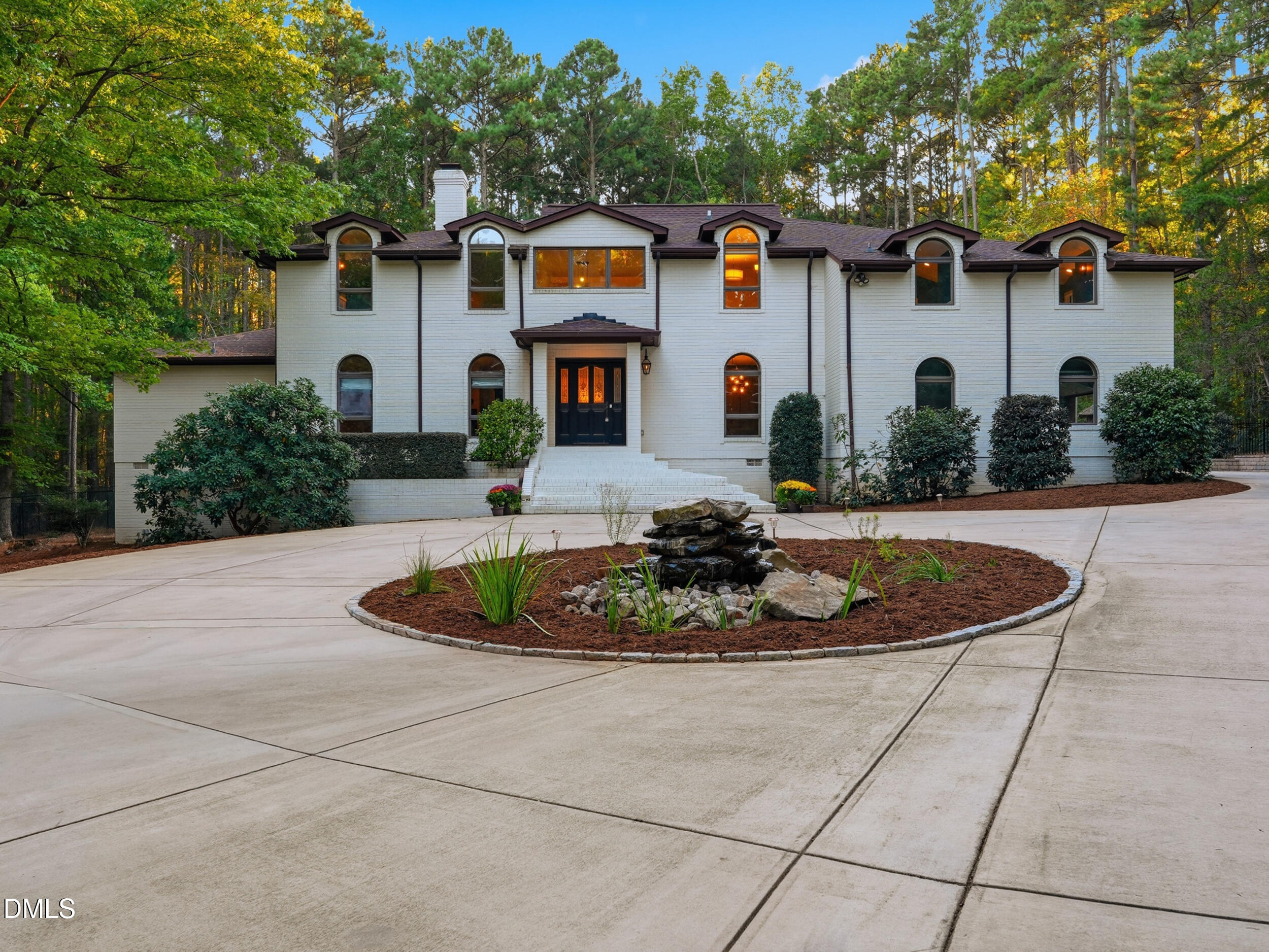 White two-story house with arched windows, a circular driveway, and a stone fountain.