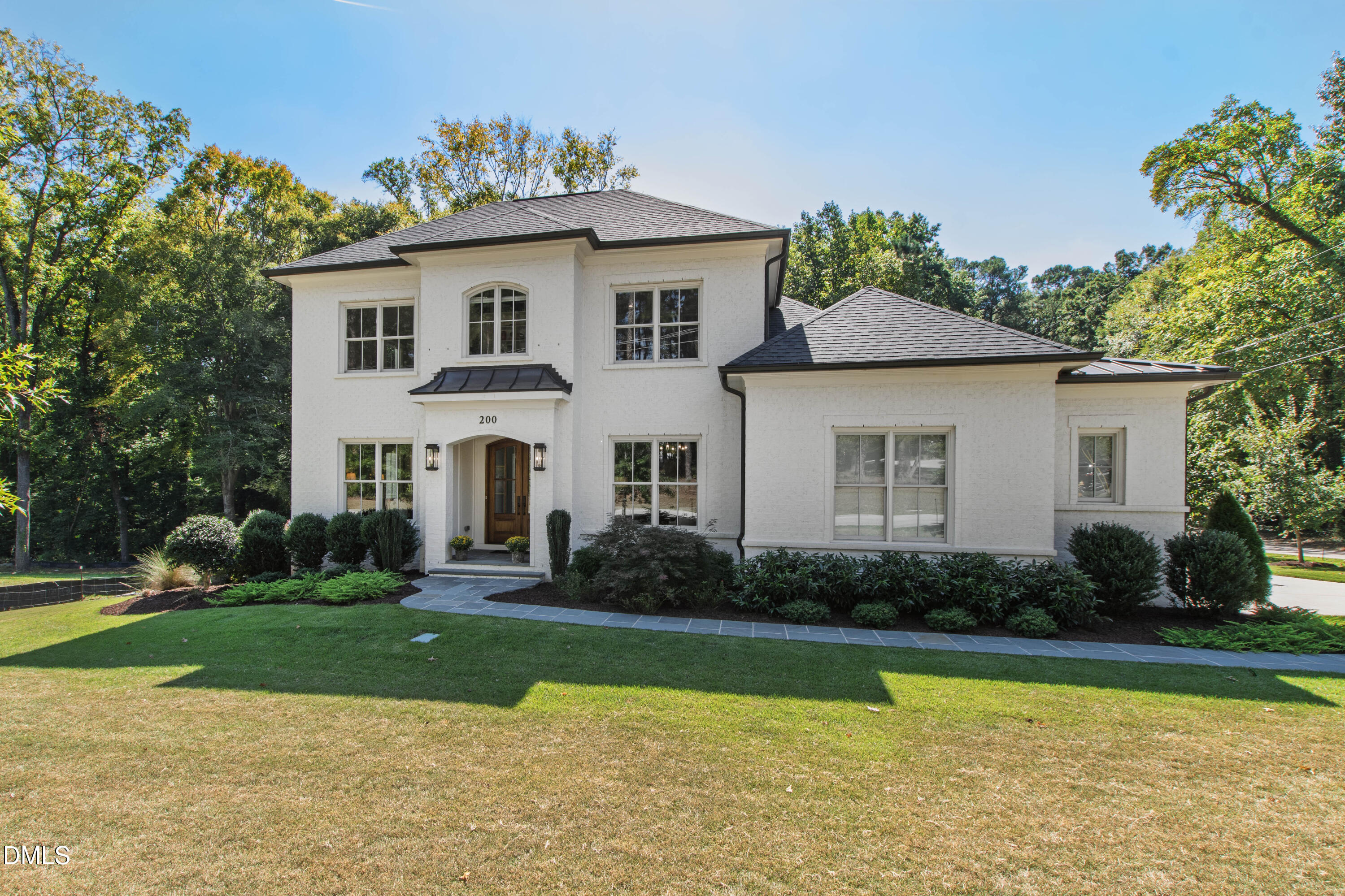 Two-story white house with a dark roof, arched window, and landscaped front lawn.