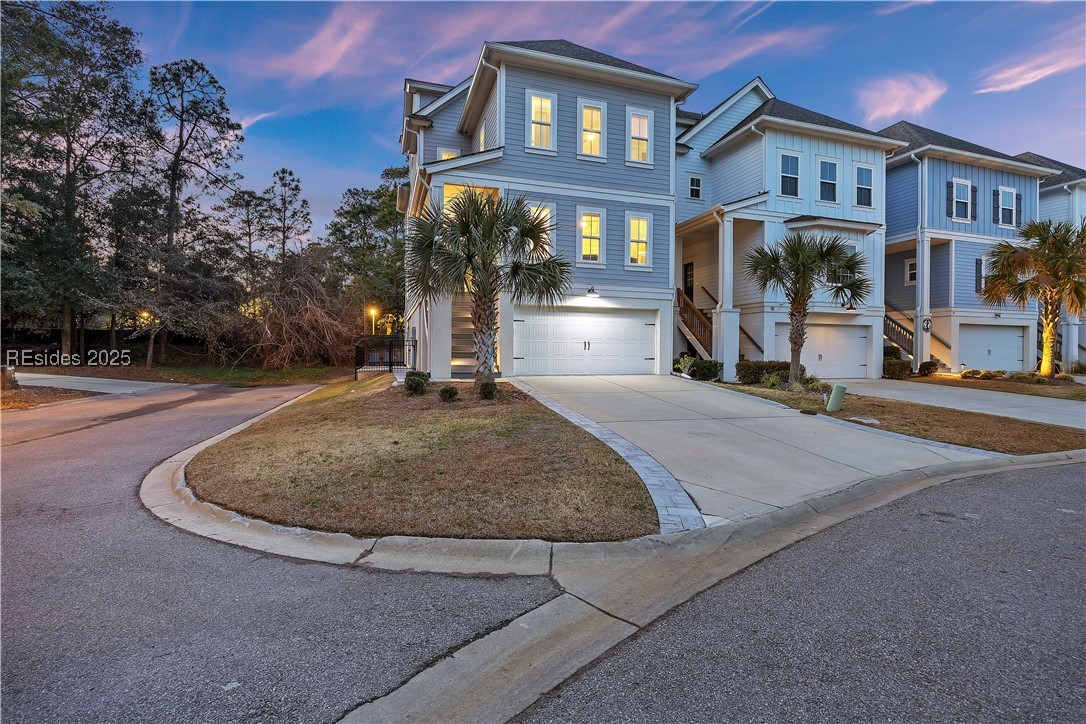 Blue multi-story home with a broad driveway and palm trees at dusk.