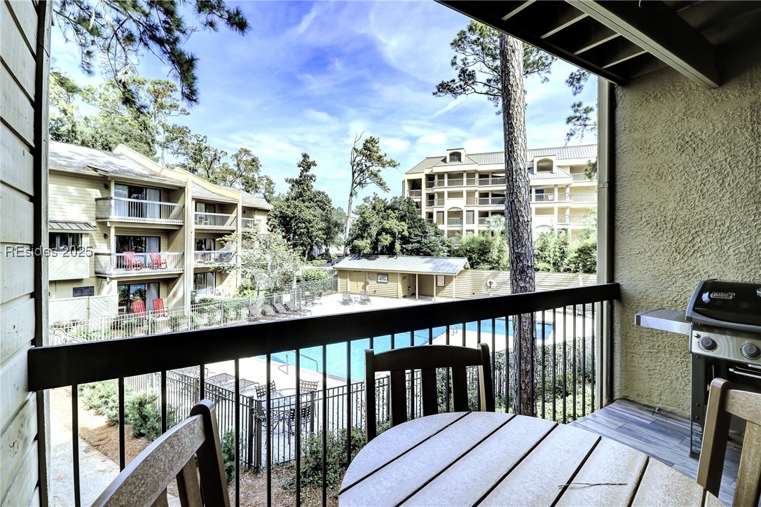 Condo balcony overlooking a swimming pool and neighboring apartment buildings, with a patio table and grill.