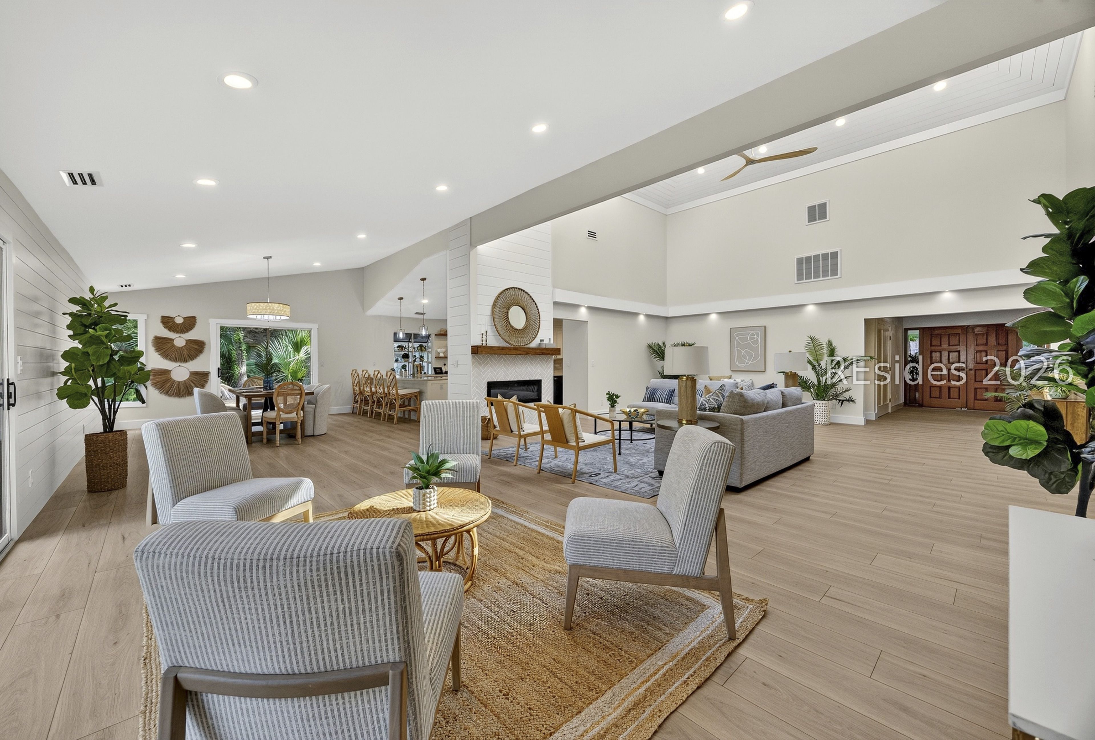 Open-plan living and dining room with a fireplace, vaulted ceiling, and light wood floors.