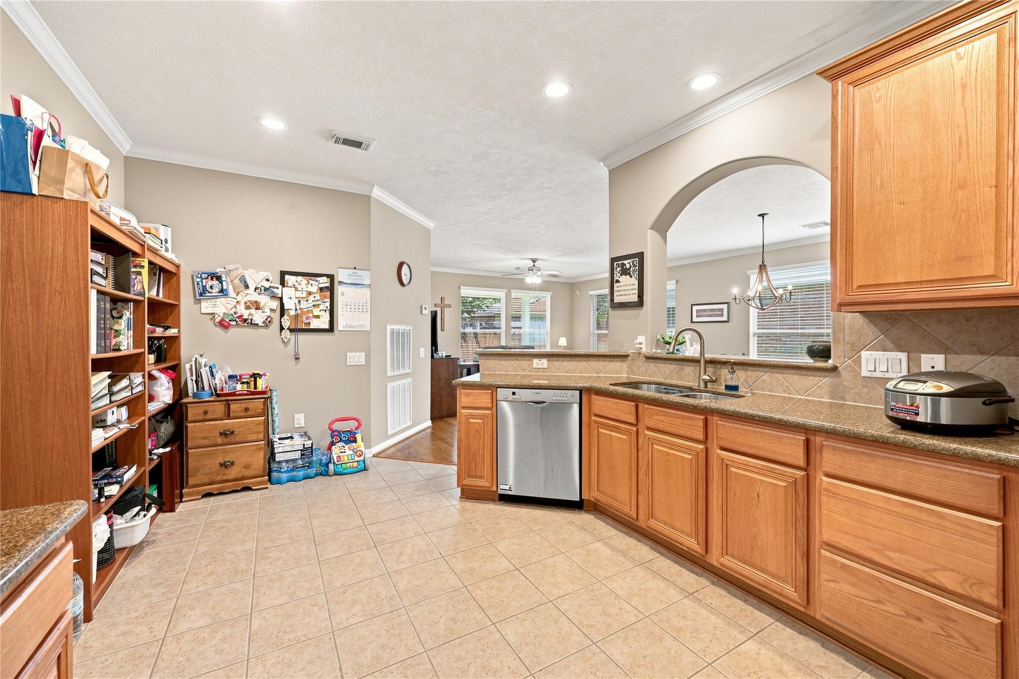 Kitchen with honey-colored cabinets, tan tile, granite counters, and a stainless-steel dishwasher.