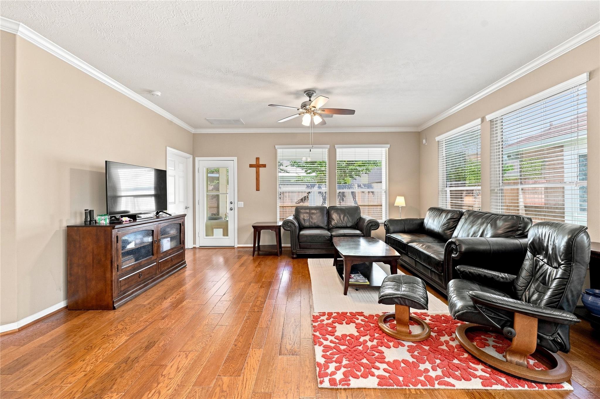 Living room with hardwood floors, black leather seating, and large windows with blinds.