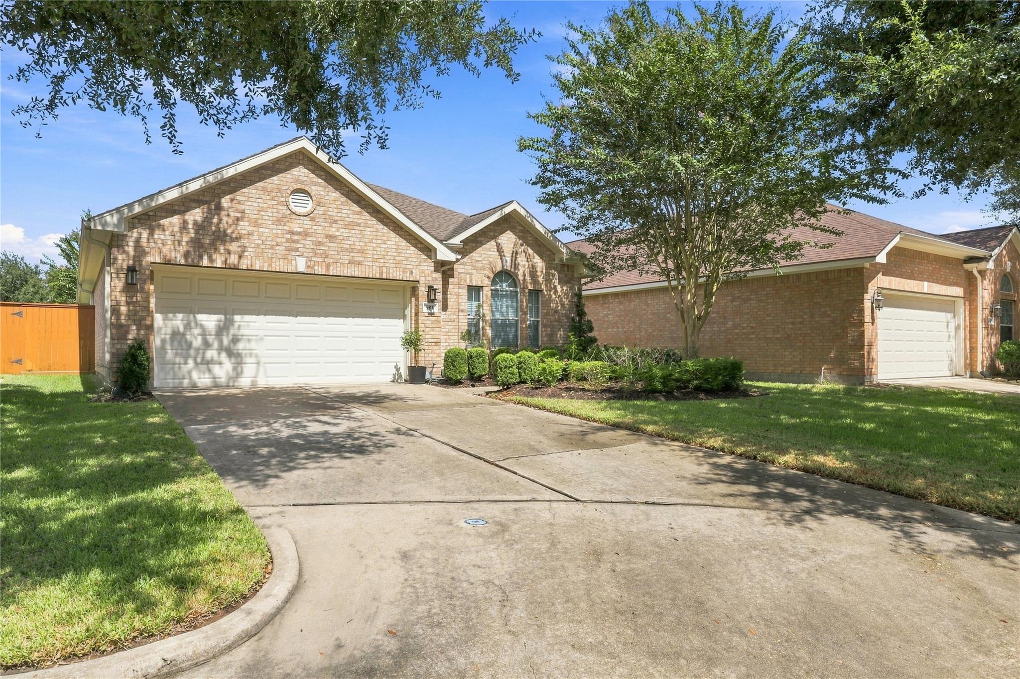 Brick home with two garage doors, a broad driveway, and mature trees.