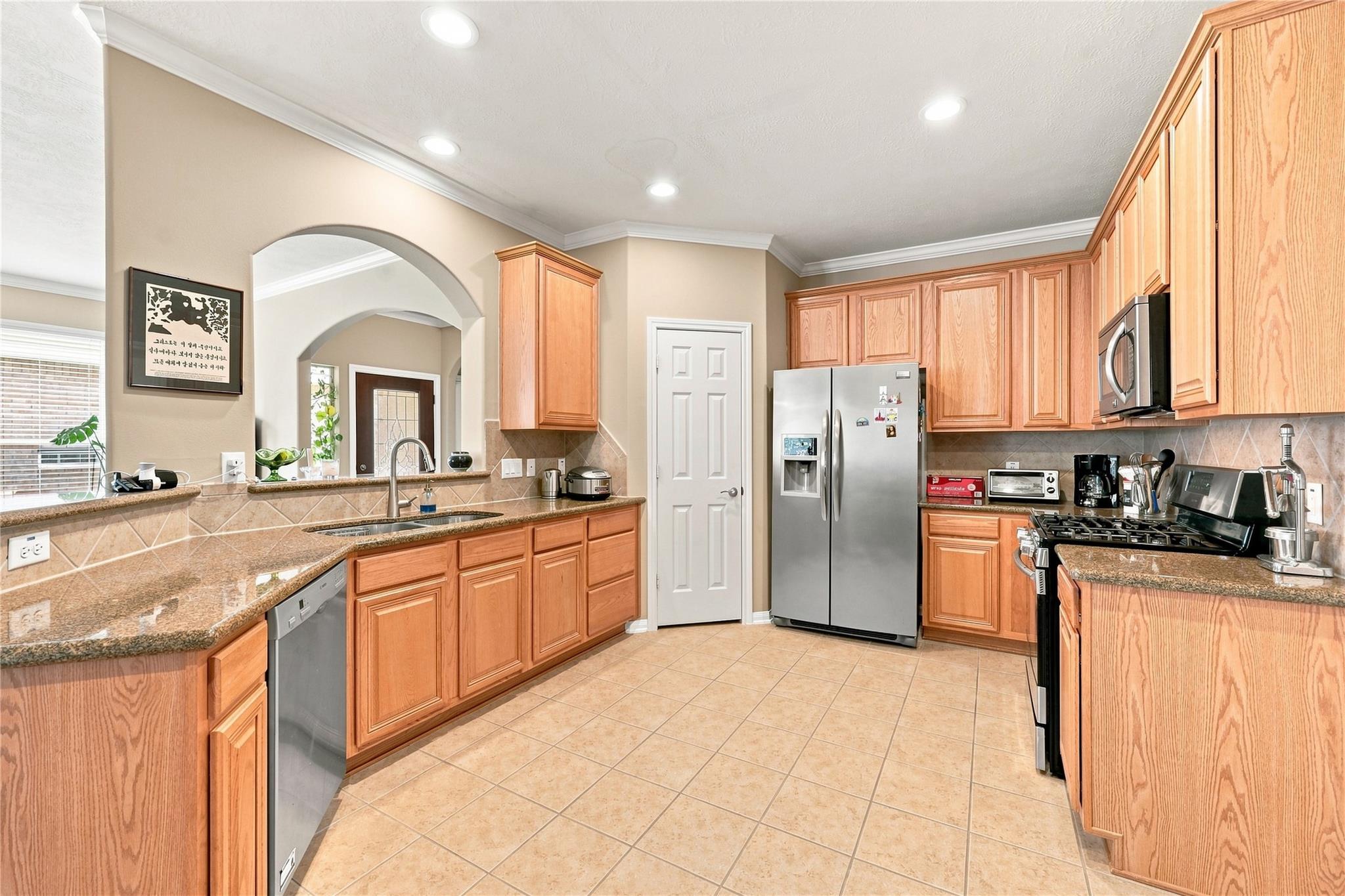 Kitchen with oak cabinets, granite counters, stainless steel appliances, and an arched opening to the entryway.