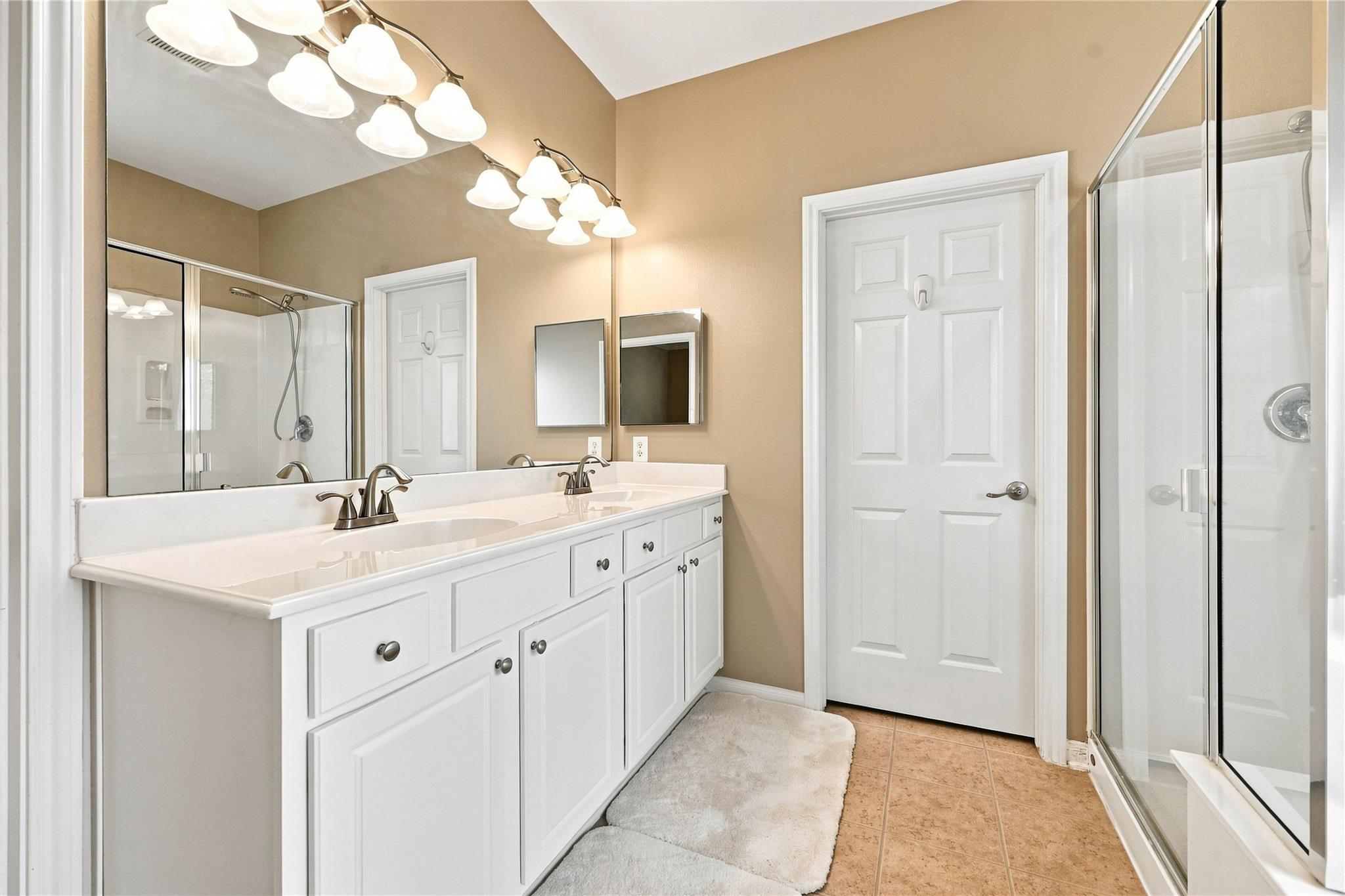 Bathroom with a white double-sink vanity, large mirrors, and glass-enclosed shower.