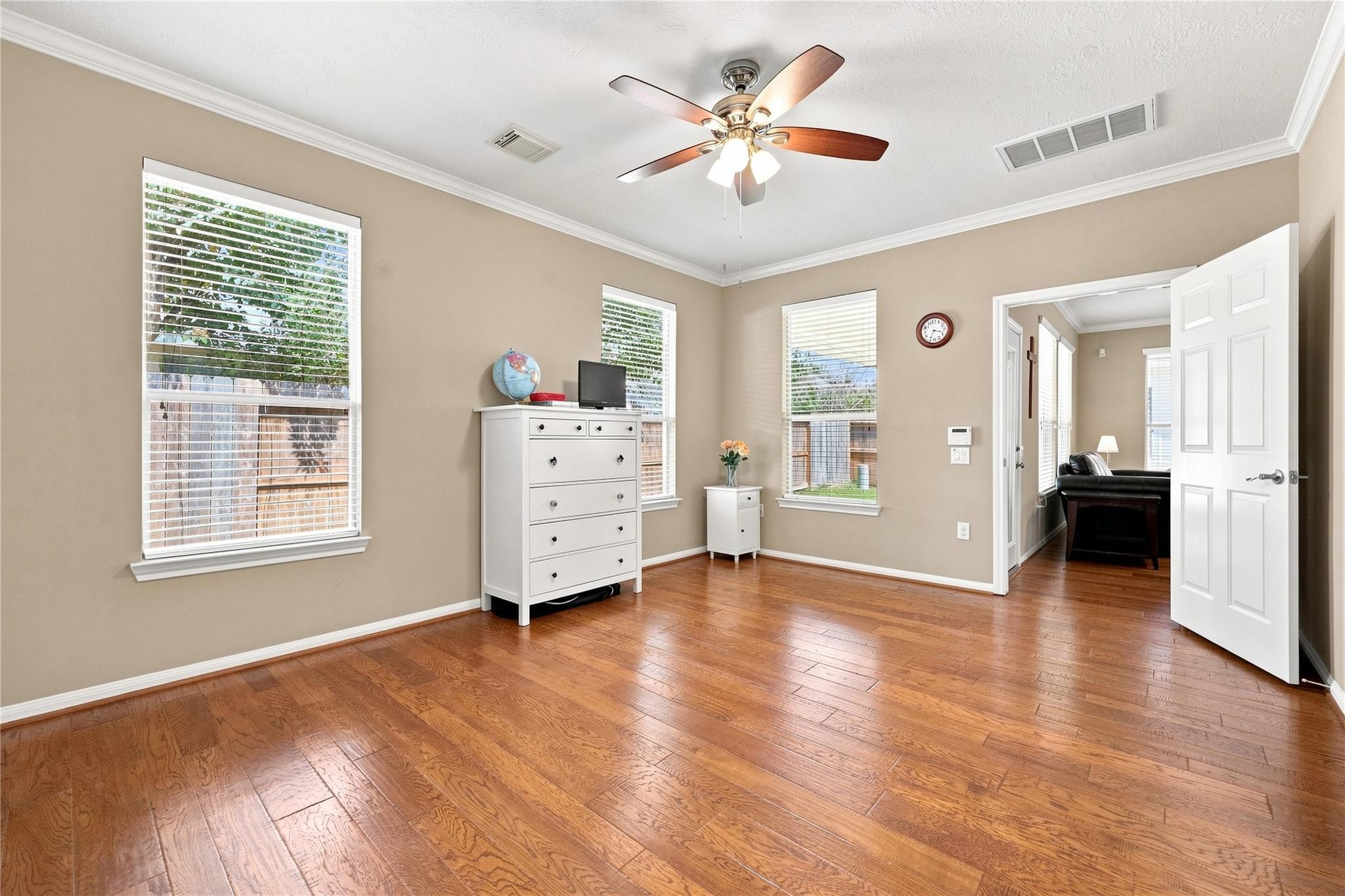 Vacant bedroom with hardwood floors, three shuttered windows, and a ceiling fan.