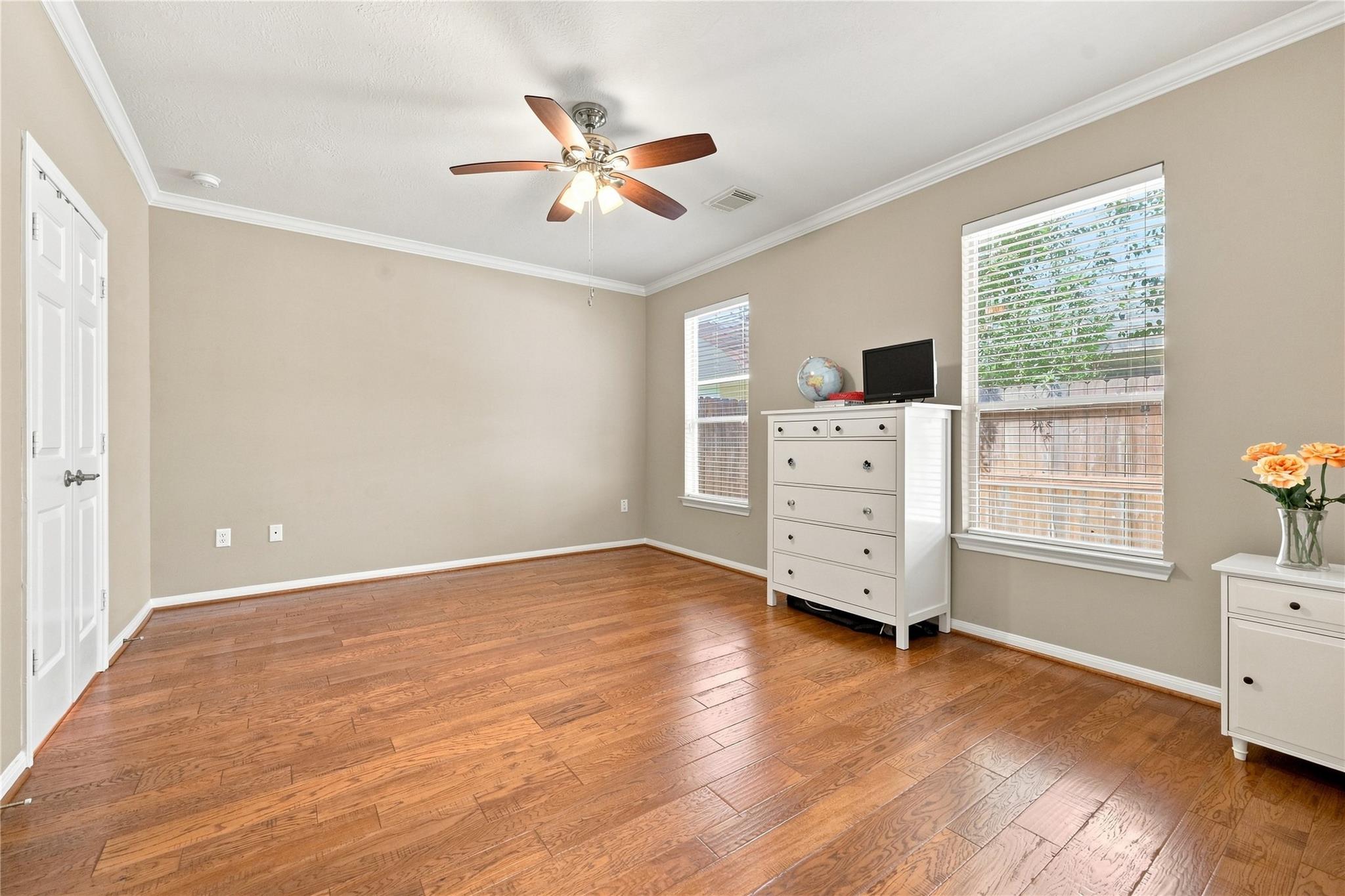 Mostly empty bedroom with hardwood floors, a ceiling fan, two windows, and a white chest of drawers.