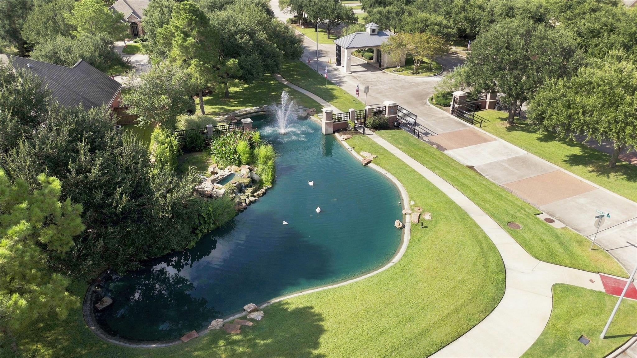 A landscaped community entrance with a fountain pond, gated walkway, and covered pavilion.