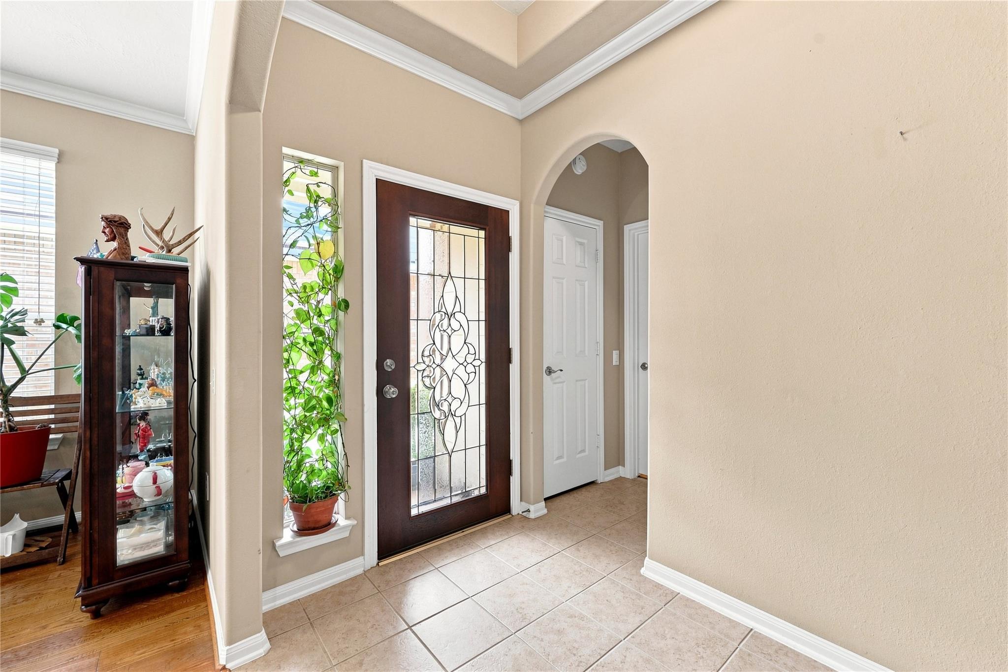 Entry foyer with a decorative glass front door, arched hallway, and leafy vine beside a narrow window.