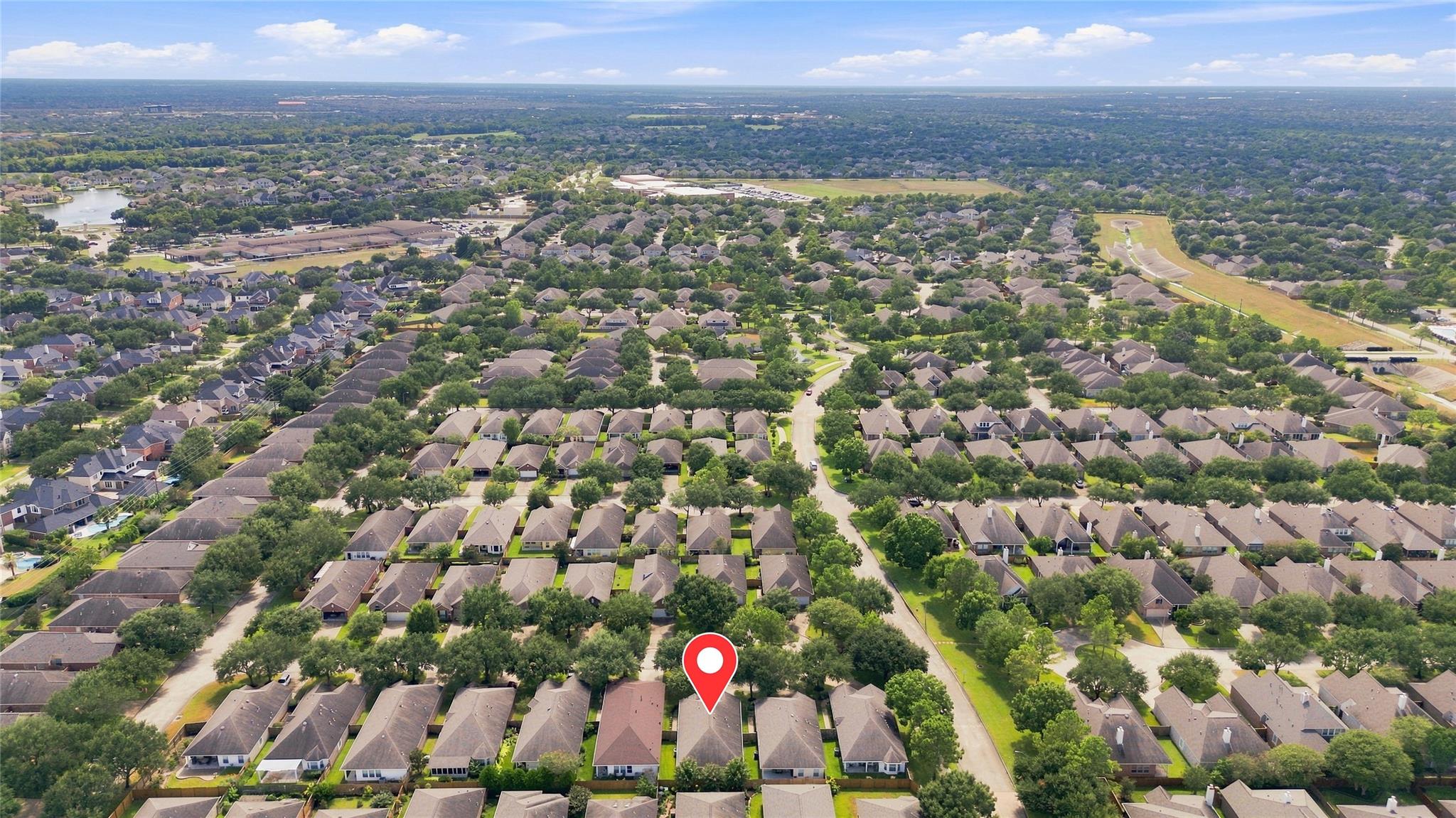 Aerial view of a leafy neighborhood, with a red location pin marking a house.