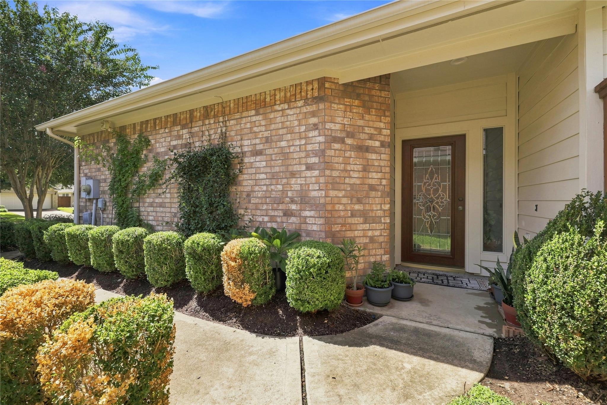 Home entrance with a brick facade, covered porch, decorative-glass door, and neatly trimmed shrubs.