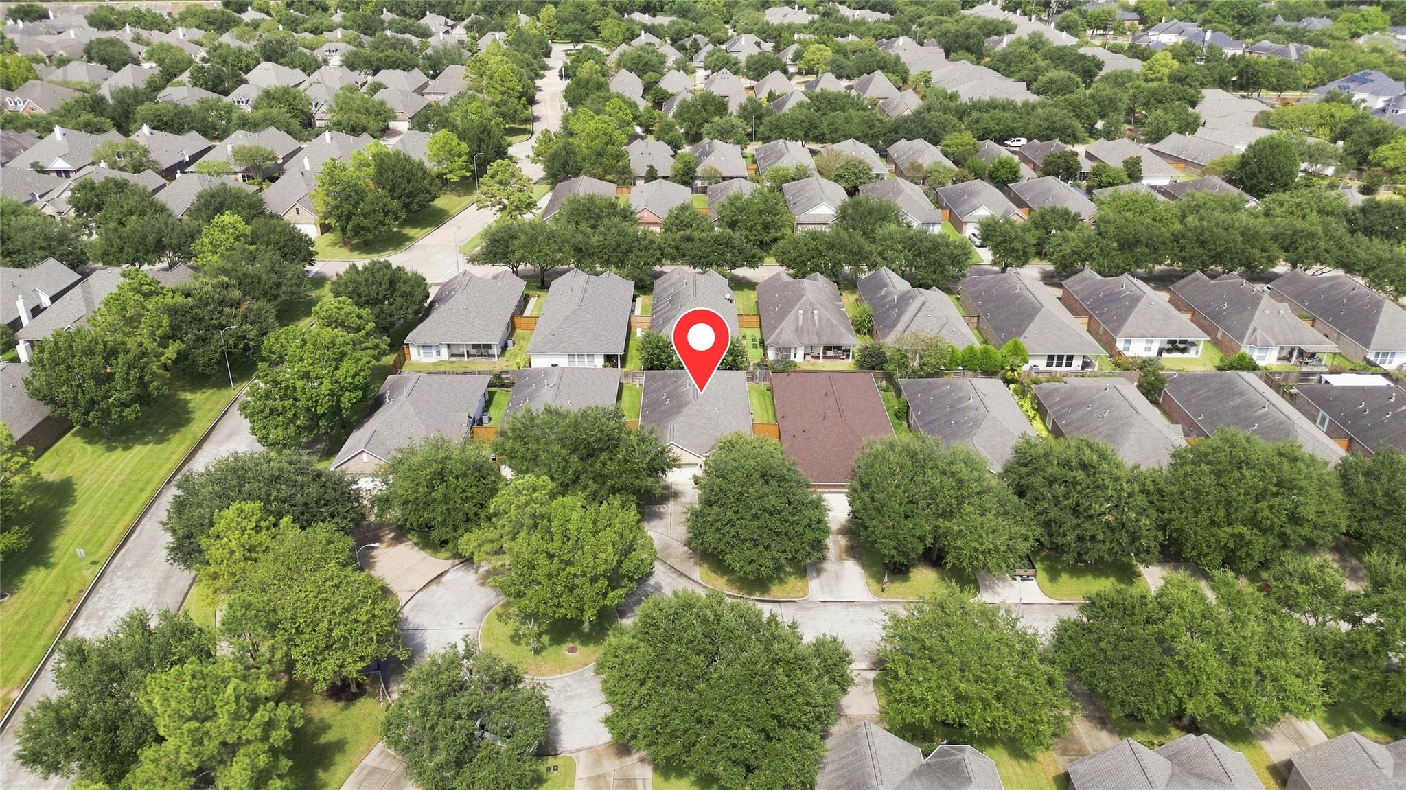 Aerial view of a tree-lined neighborhood, with a red pin marking a gray-roofed home.