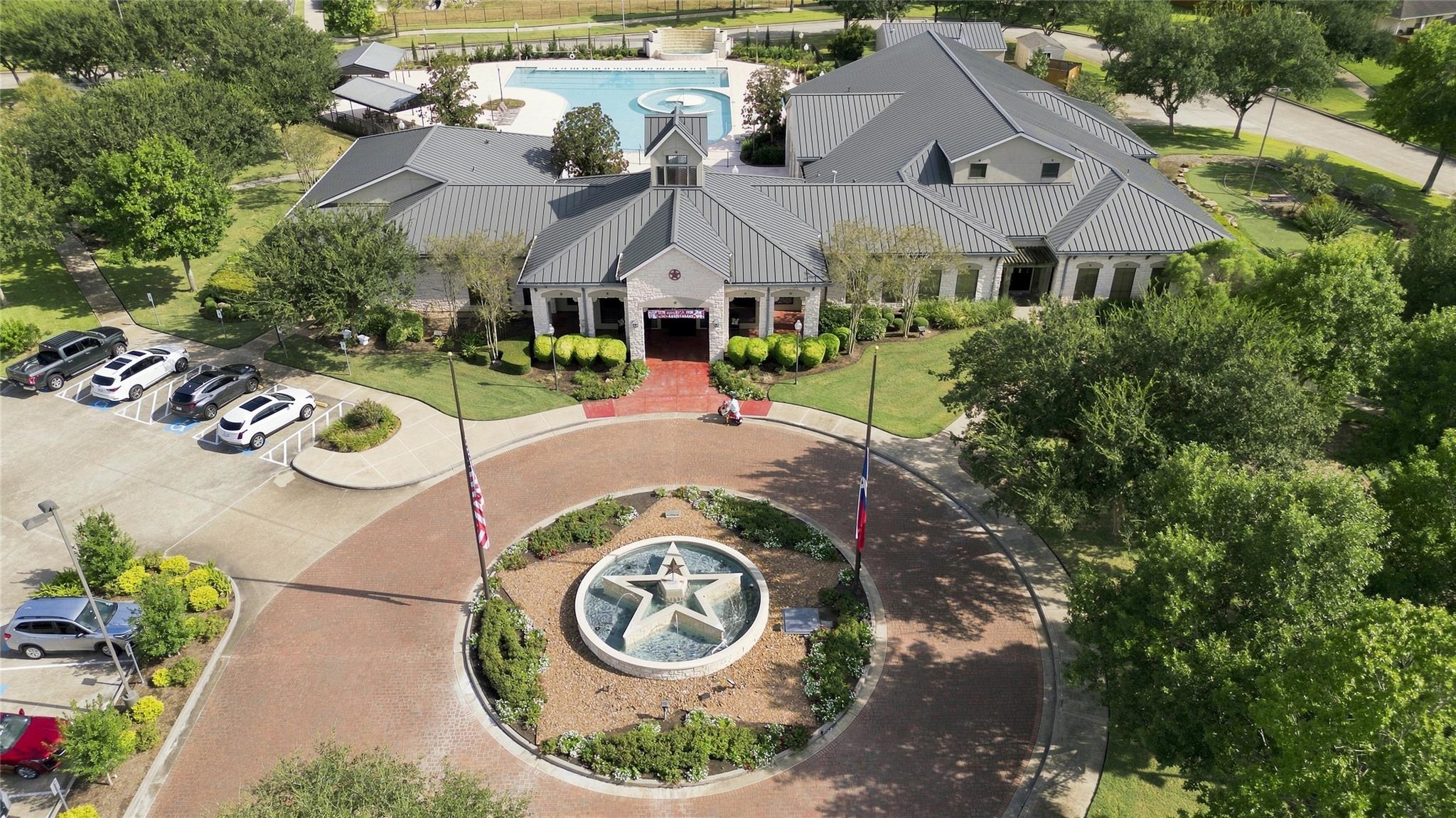 Community clubhouse and pool viewed from above, with a star-shaped fountain in the circular drive.