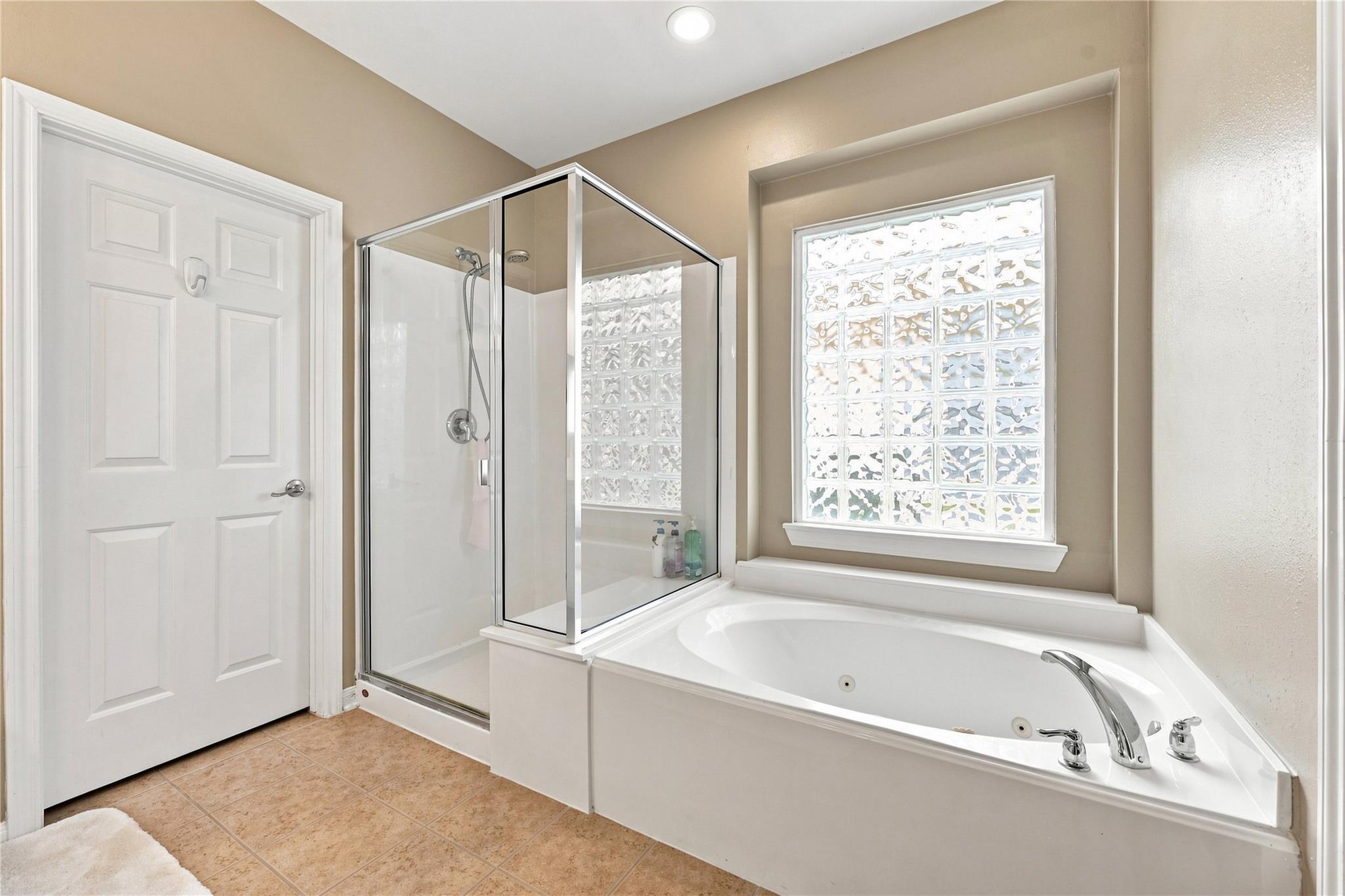 Bathroom with a corner soaking tub, glass-enclosed shower, and large glass-block window.