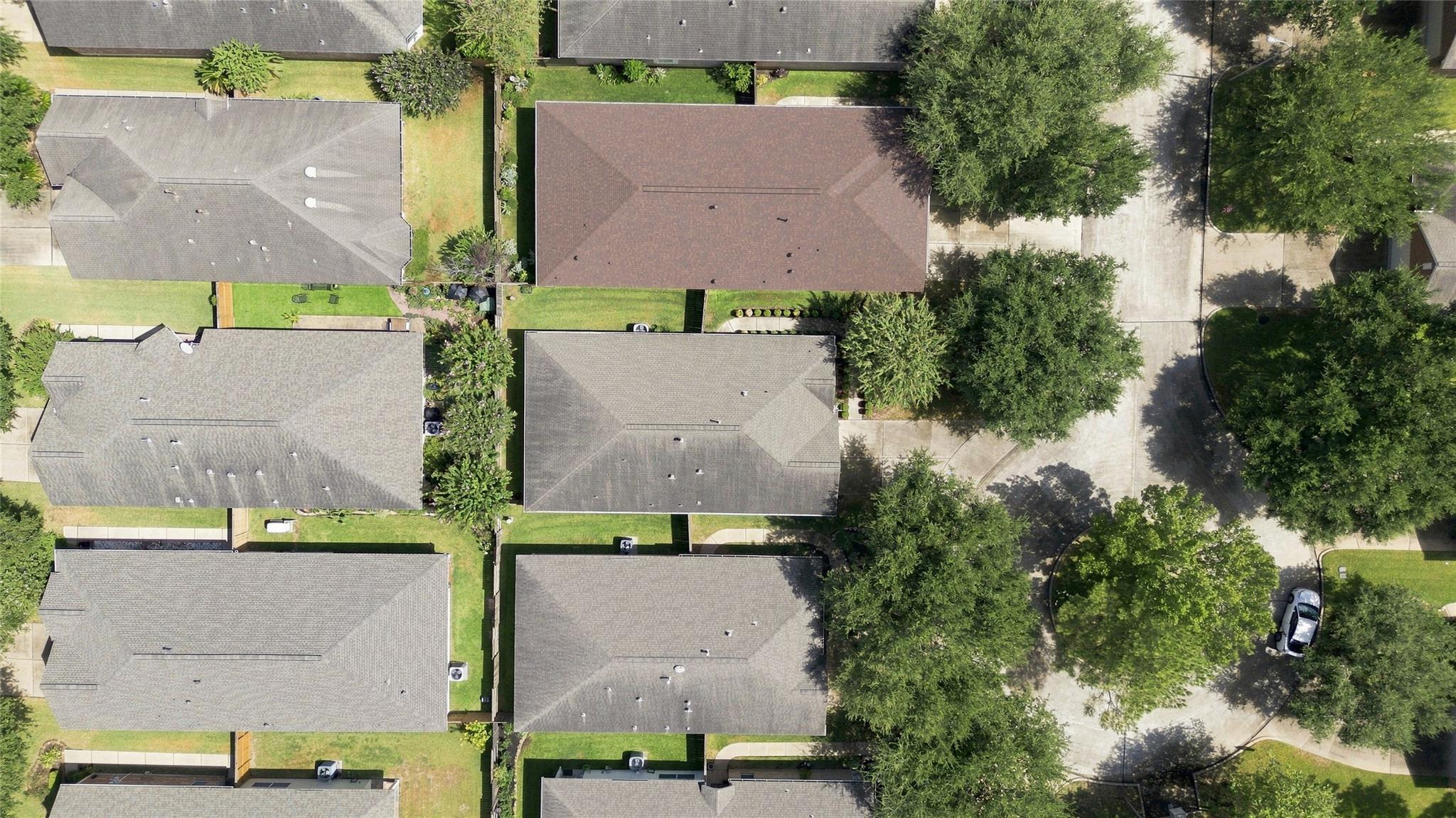 Aerial view of a brown-roofed home among neighboring houses and mature trees.