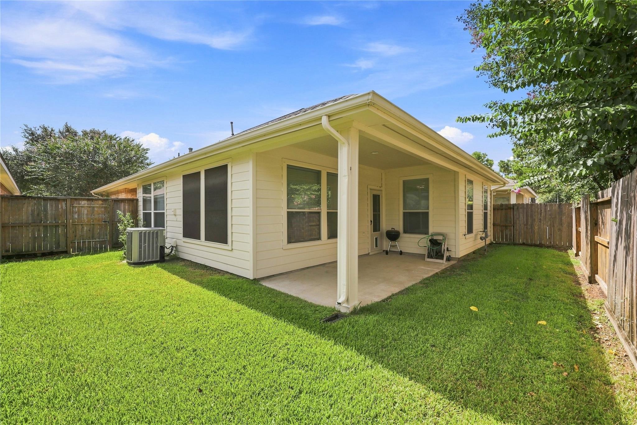Rear of a light-colored house with a covered patio and fenced grassy backyard.