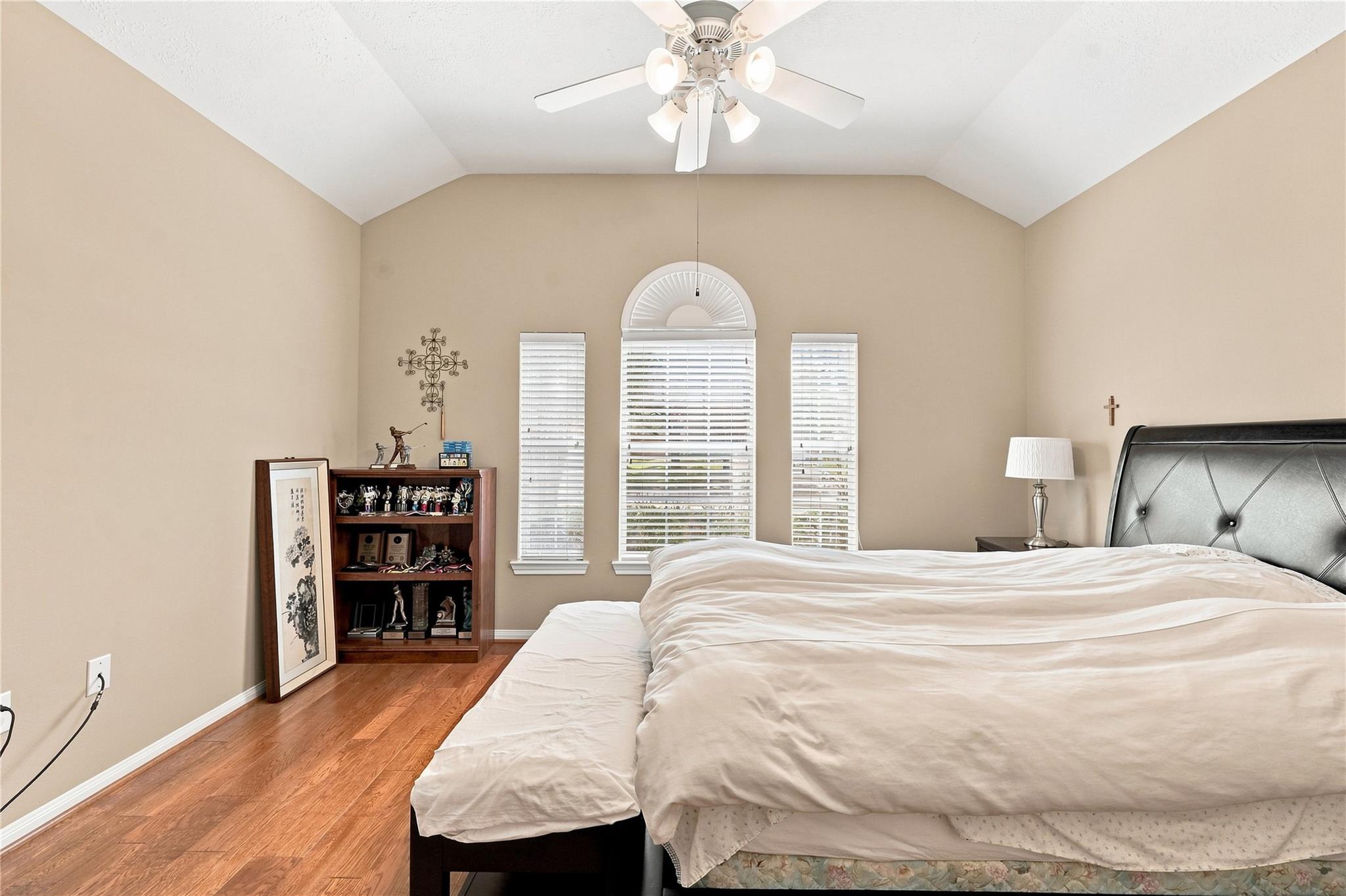 Bedroom with a vaulted ceiling, arched window, hardwood floors, and a large bed.