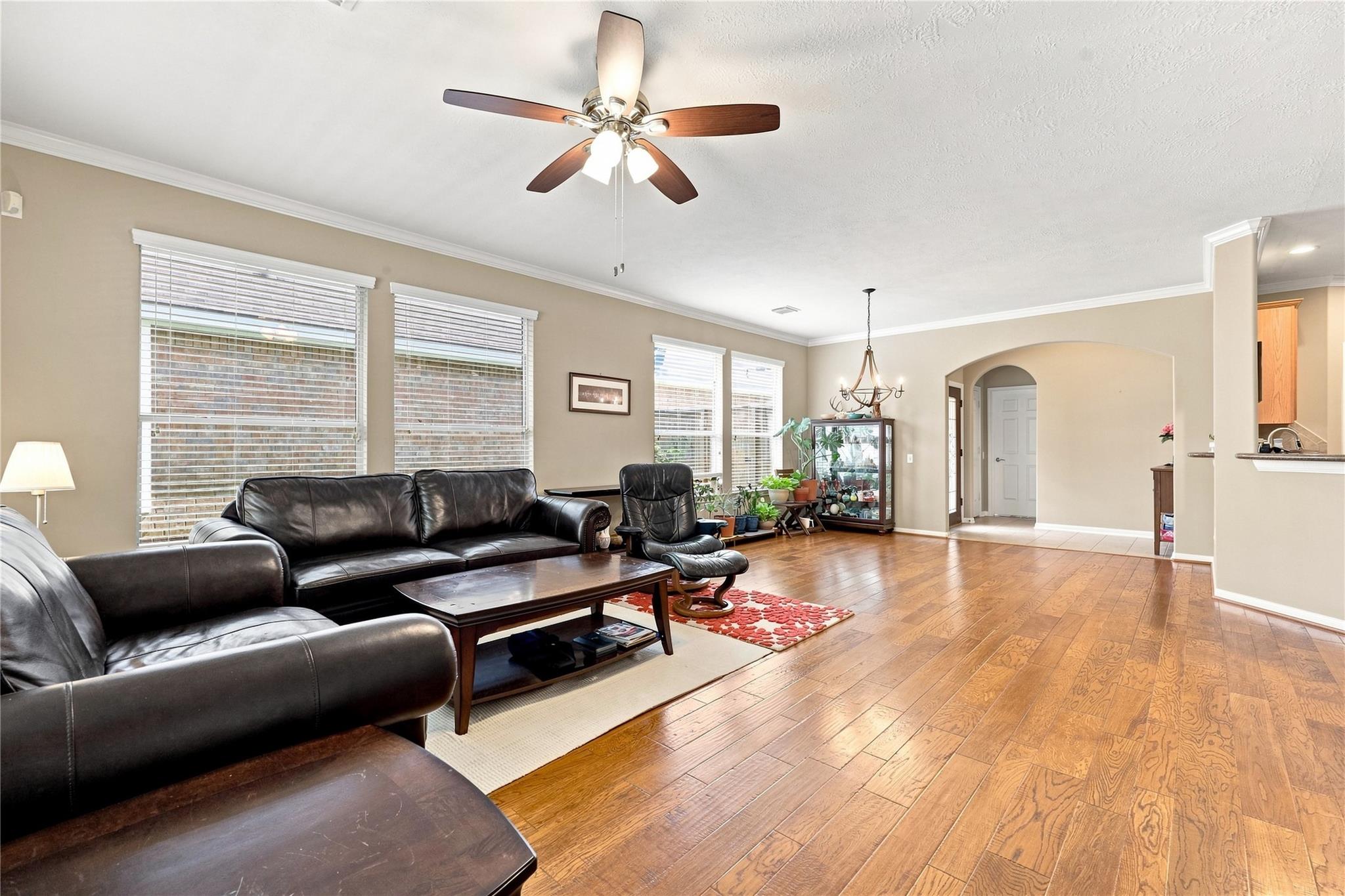 Living room with dark leather seating, hardwood floors, and a ceiling fan.